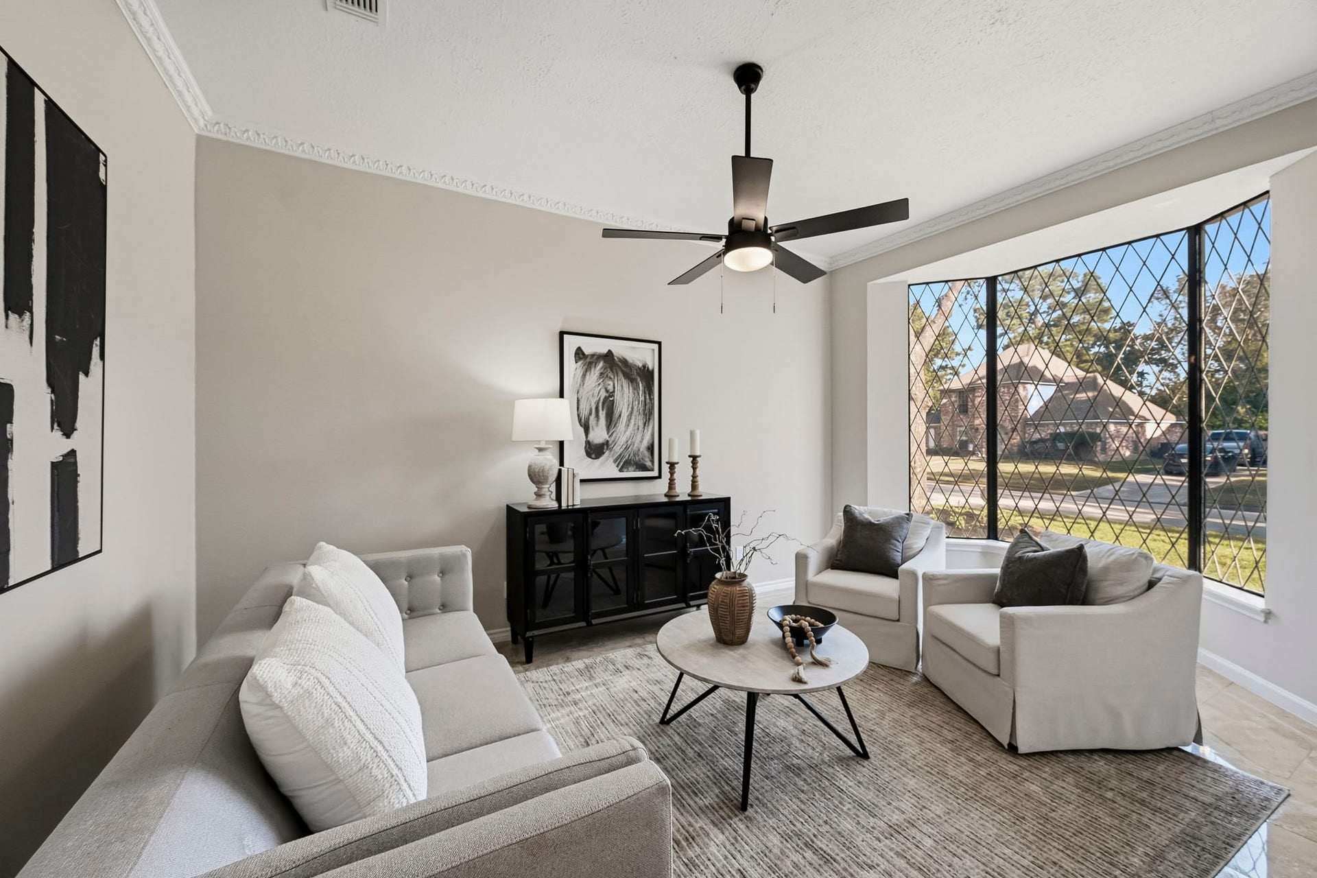6714 Brittany Park Lane, Houston, TX 77066 Charming living room with a modern ceiling fan, large diamond-patterned windows allowing natural light, and stylish neutral furnishings creating an inviting atmosphere.