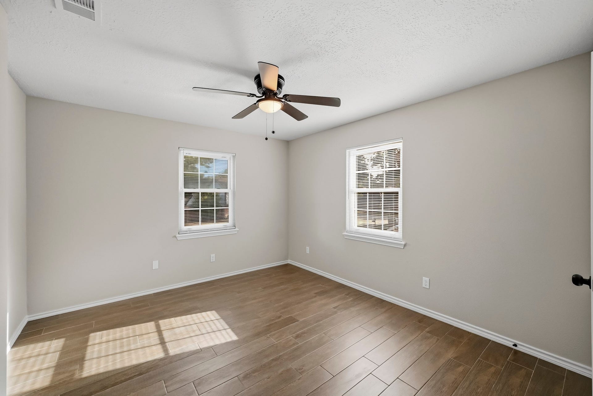 6714 Brittany Park Lane, Houston, TX 77066 Bright and inviting bedroom featuring sleek wood-look tile flooring, neutral walls, and a modern ceiling fan, with ample natural light from two windows.