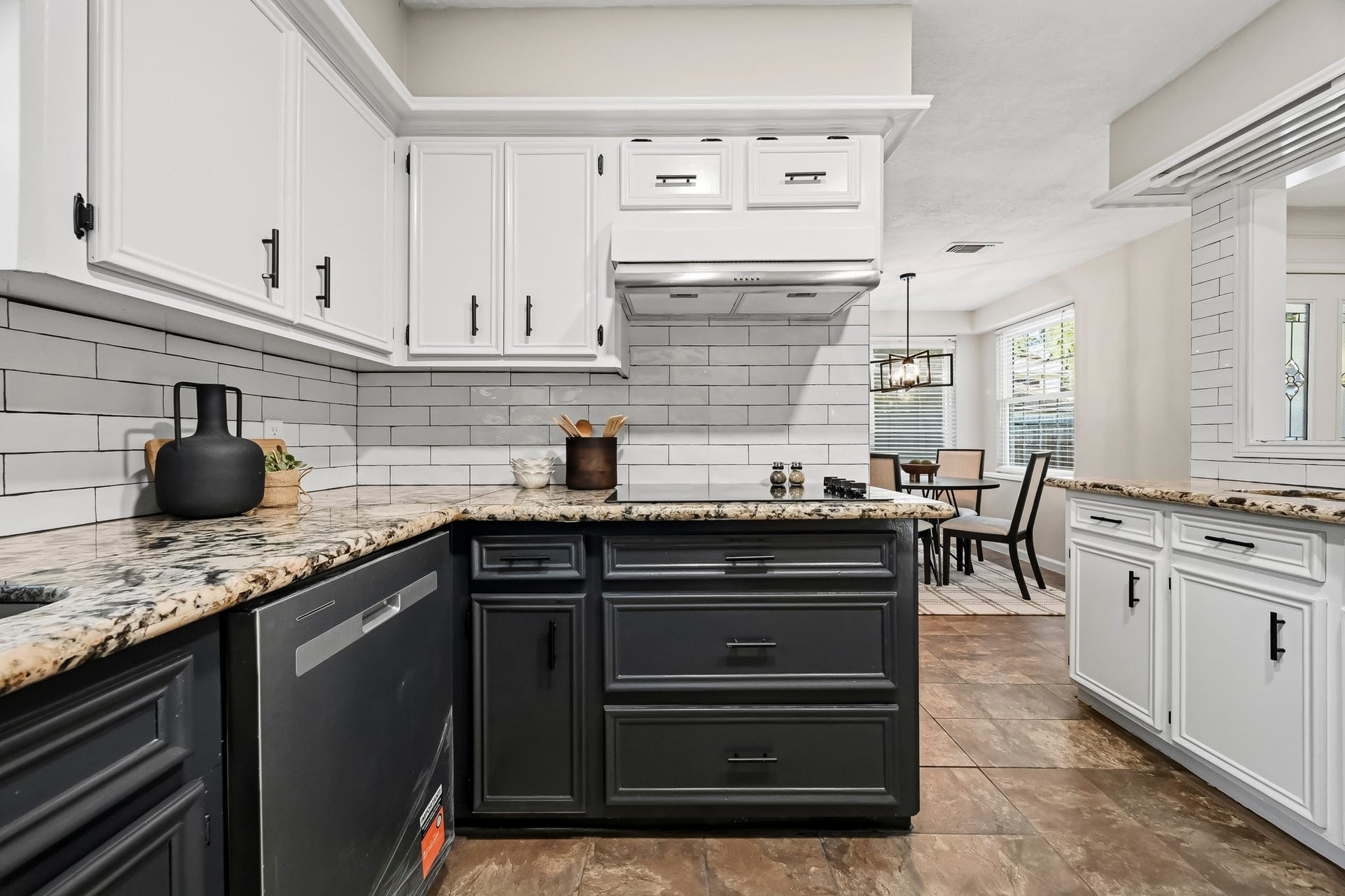 6714 Brittany Park Lane, Houston, TX 77066 Stylish kitchen featuring a modern two-tone design with sleek black and white cabinetry, granite countertops, and a subway tile backsplash, seamlessly flowing into a bright dining area.