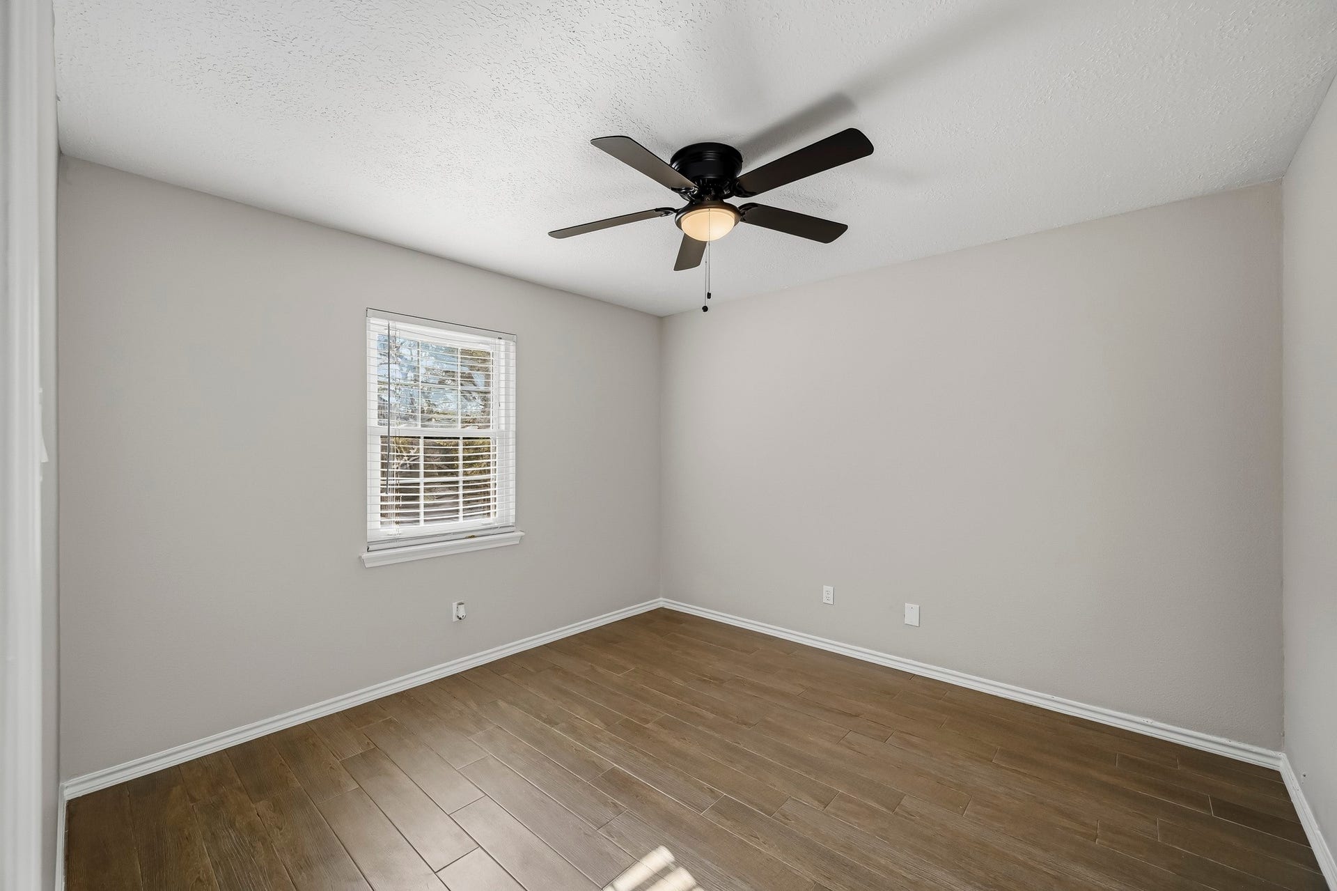 6714 Brittany Park Lane, Houston, TX 77066 Bright and inviting bedroom featuring sleek wooden floors, a modern ceiling fan, and ample natural light through a large window.