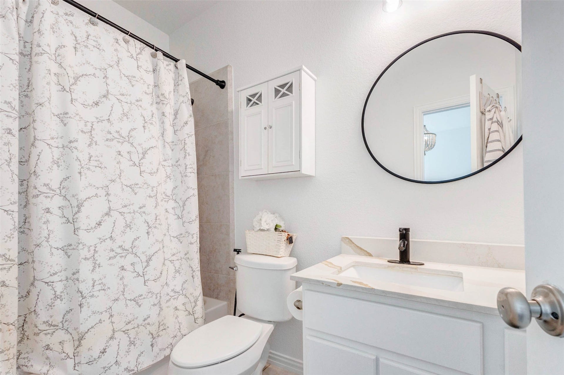 A clean and well-appointed secondary bathroom features modern touches and a functional layout. The shower and tub combination is complemented by stylish fixtures and a light, neutral palette. A sleek vanity with storage and a round mirror adds contemporary flair, while thoughtful details make this space both practical and visually appealing for everyday use.