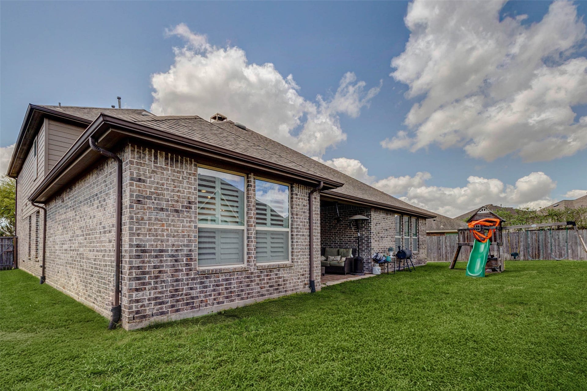 This spacious backyard offers plenty of room to play, relax, and entertain. The green lawn provides open space for outdoor activities, while the covered patio offers a shaded place to unwind. The yard includes a playset. Fully fenced for privacy, it's a functional outdoor retreat.