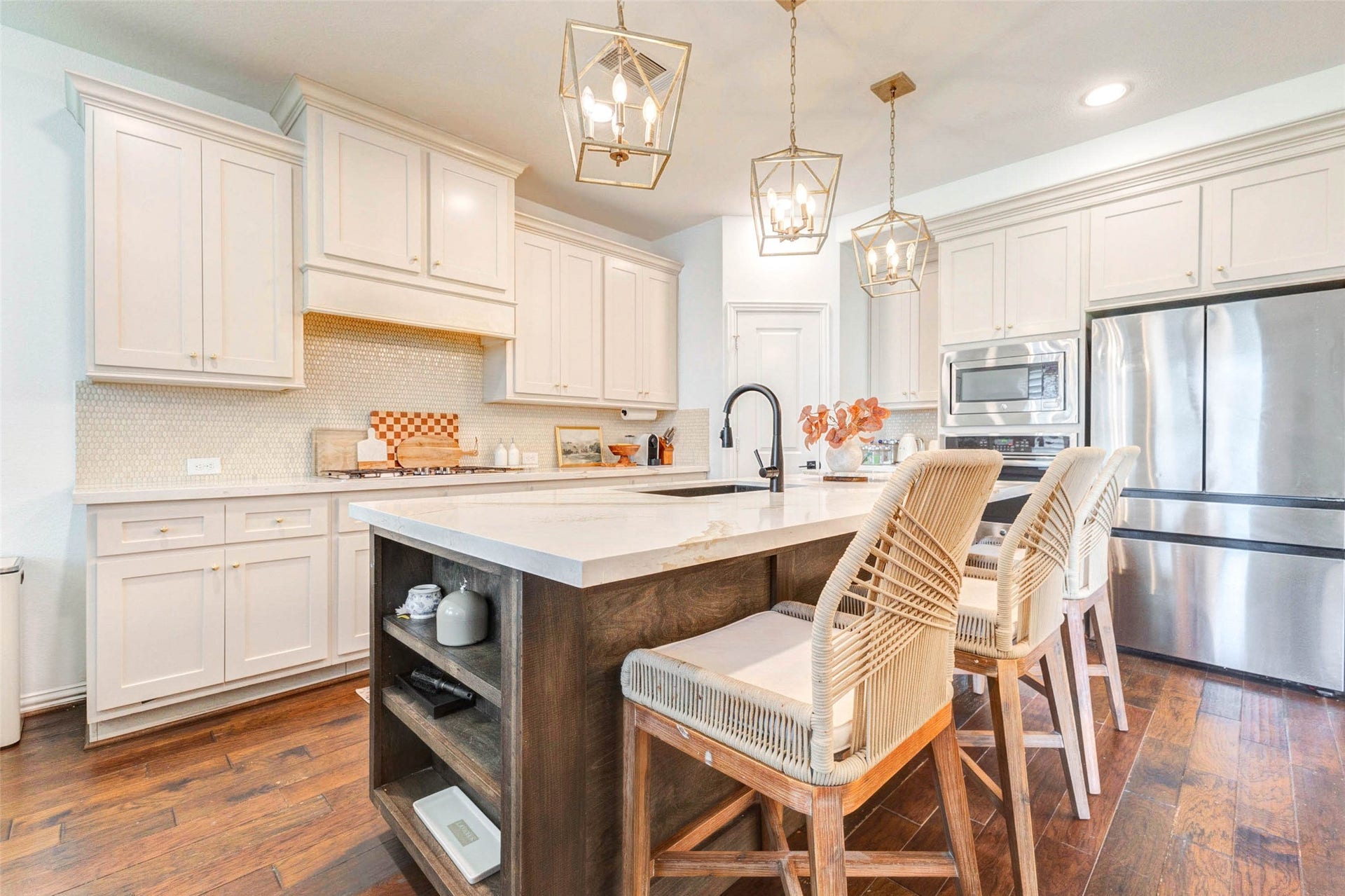 This beautifully designed kitchen showcases high-end finishes and attention to detail, from the sleek upgraded countertops to the upgraded custom cabinetry. The oversized island offers additional prep space and seating, making it the centerpiece of the room. Stainless steel appliances and a stylish backsplash complete the look, while the warm wood tones and neutral palette create a welcoming and sophisticated atmosphere.