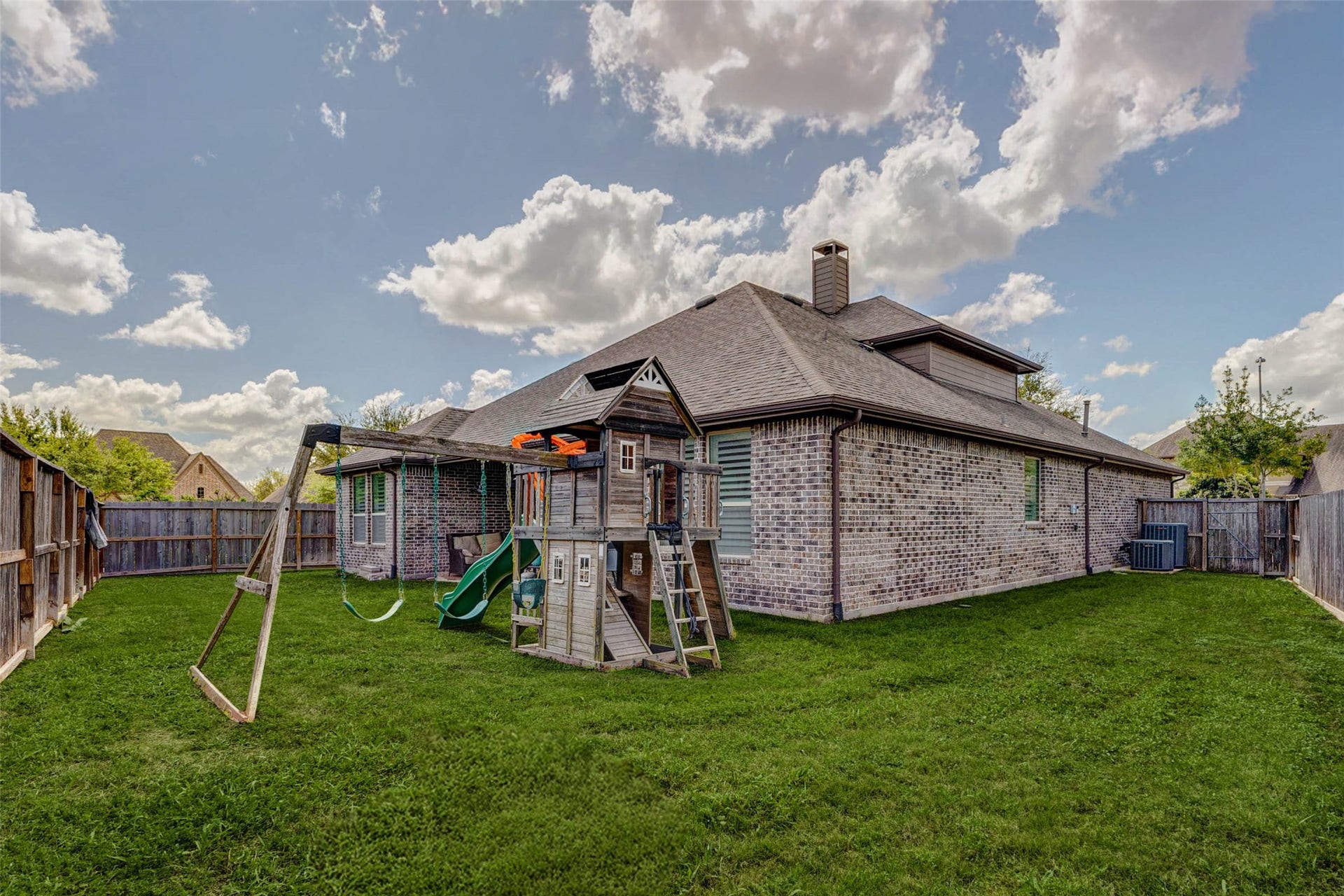 A wide-angle view showcases the expansive backyard and the homes beautiful brick exterior. The generous lawn space is perfect for gatherings, play, or gardening, while the covered patio creates a seamless indoor-outdoor living experience. With plenty of room to enjoy and personalize, this backyard offers both privacy and versatility for everyday living.