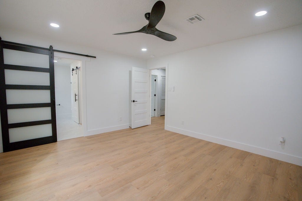 Spacious room featuring sleek vinyl floors, a modern ceiling fan, and stylish barn doors leading to an adjoining space.