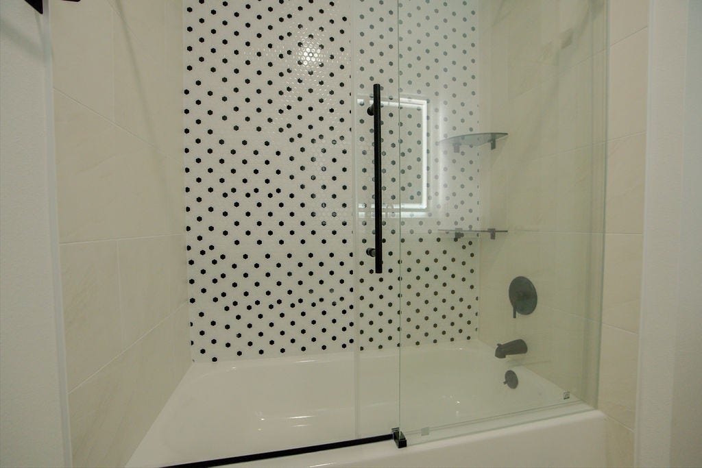 Sleek bathroom featuring a modern shower with stylish black and white polka dot tile, complemented by a glass door and matte black fixtures.