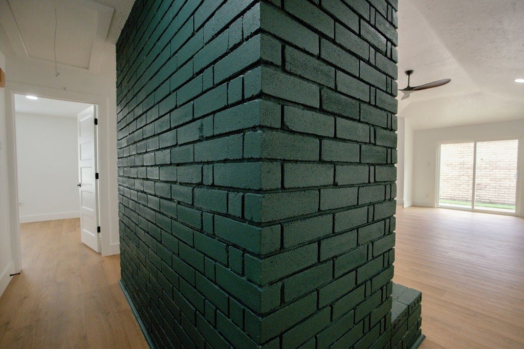 Chic and modern interior featuring a striking dark green brick accent wall, light wood style flooring, and ample natural light pouring through large sliding glass doors.