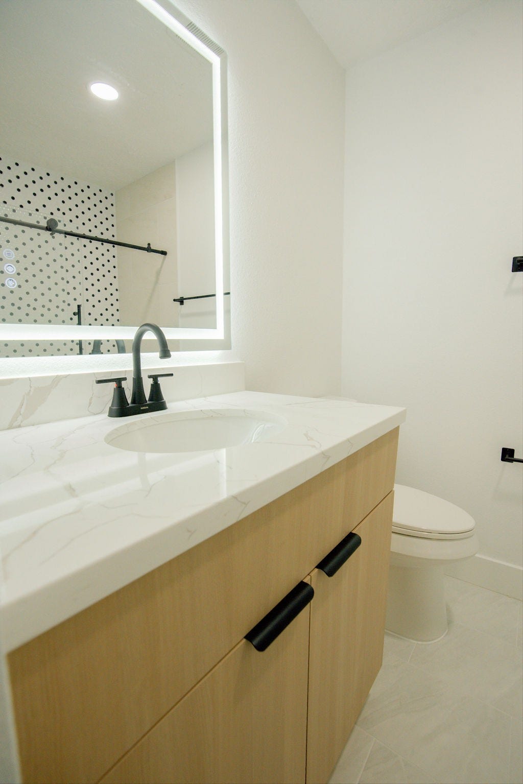 Modern bathroom featuring a sleek vanity with a quartz countertop, stylish black fixtures, and a backlit mirror.