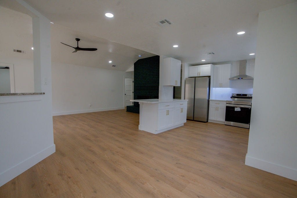Spacious open-concept living area with sleek hardwood style floors, modern kitchen featuring stainless steel appliances, and elegant recessed lighting.