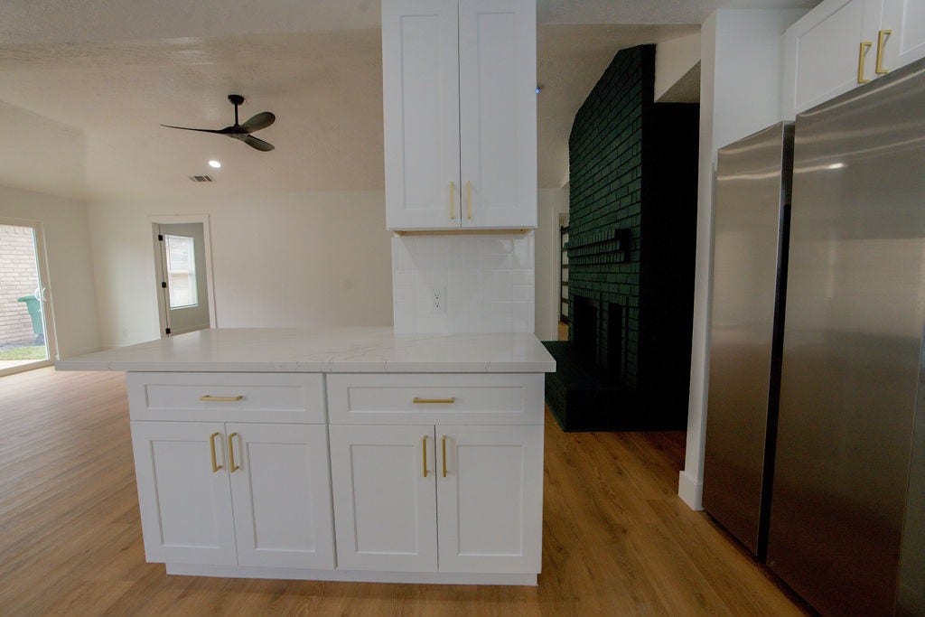 Bright and modern kitchen with sleek white cabinetry, elegant gold hardware, and a spacious island, complemented by stainless steel appliances and warm wood style flooring.