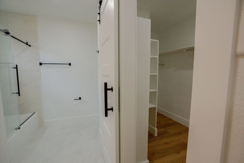 Modern bathroom with a sleek glass-enclosed shower, adjacent to a spacious walk-in closet featuring built-in shelving and ample hanging space.