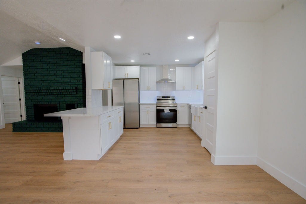 Bright and modern kitchen with sleek white cabinetry, stainless steel appliances, and a stylish dark fireplace accenting the open-concept layout.
