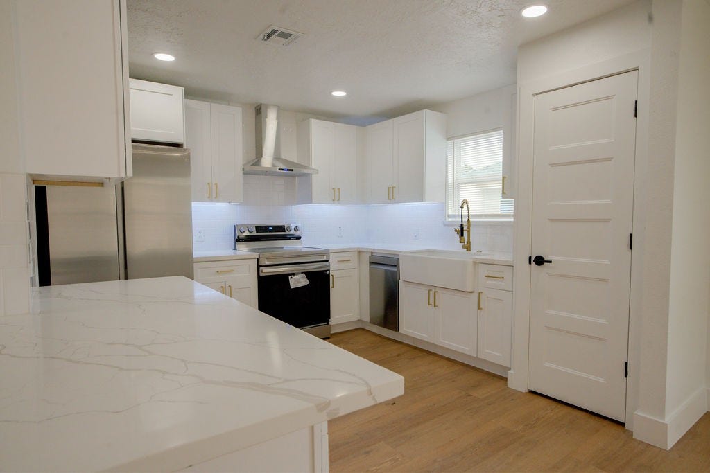 Sleek and modern kitchen featuring white cabinetry, stainless steel appliances, a farmhouse sink, and elegant quartz countertops.