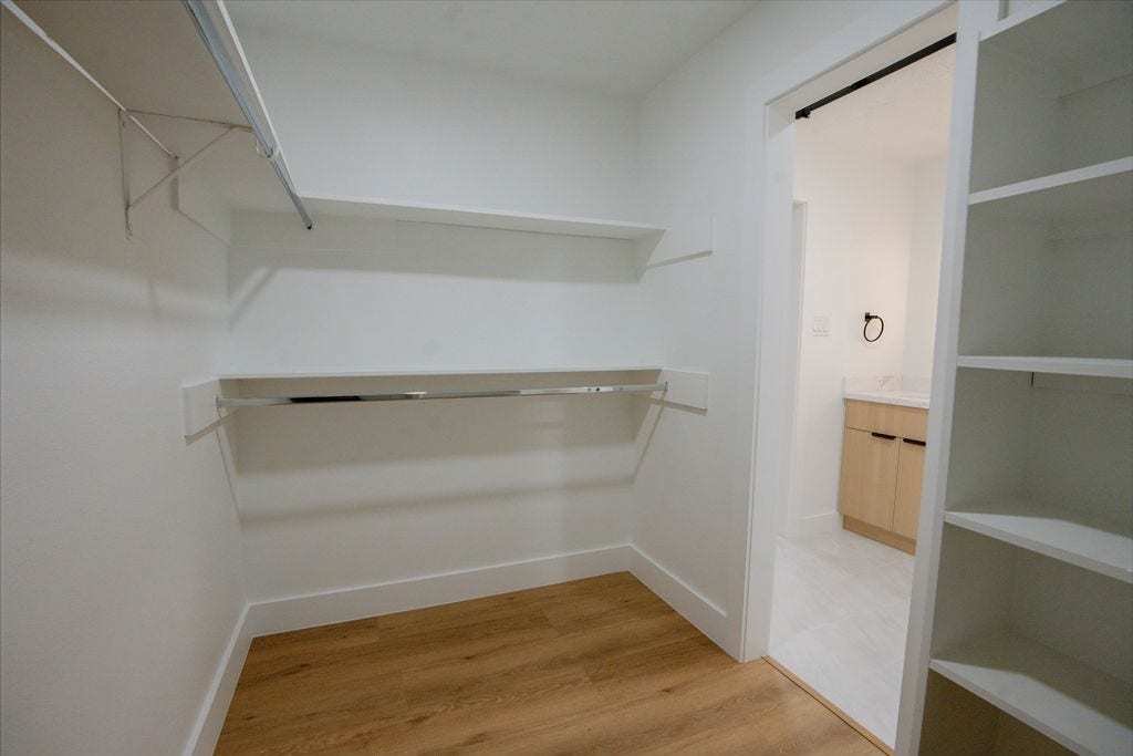 Spacious walk-in closet with ample shelving and hanging space, featuring elegant wood style flooring and convenient access to the adjoining bathroom.