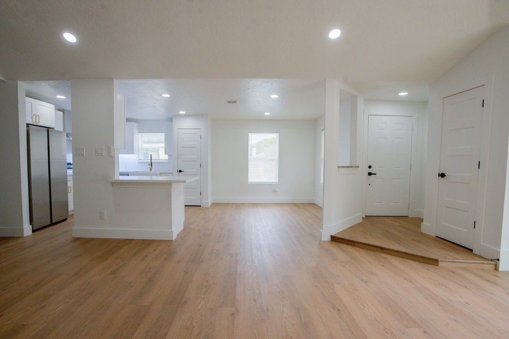 Bright and spacious open-concept living area with sleek vinyl floors, recessed lighting, and a modern kitchen featuring stainless steel appliances.