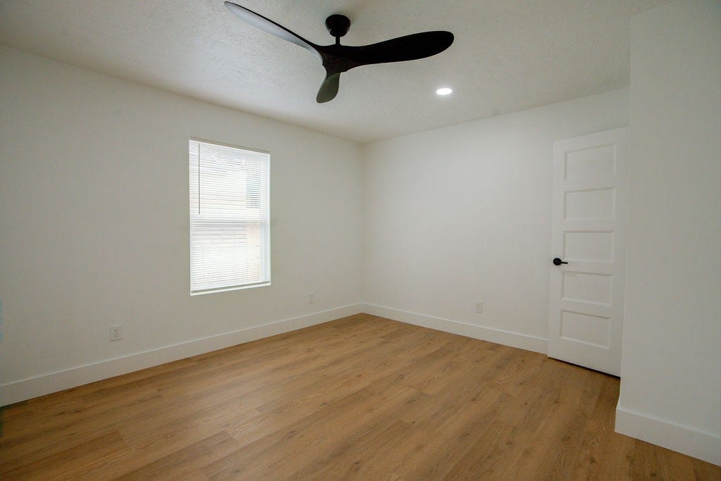 Bright, minimalist room with sleek vinyl floors, a modern ceiling fan, and ample natural light from a large window.