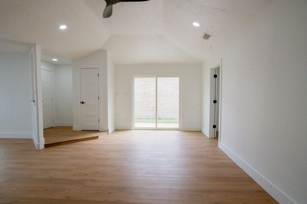 Bright and spacious room featuring high ceilings, recessed lighting, and elegant wood style flooring, with sliding doors leading to a private outdoor area.