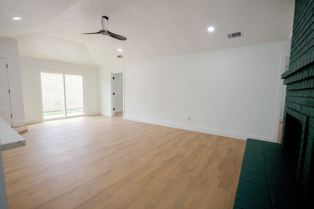 Spacious, bright living area with sleek vinyl floors, a modern ceiling fan, and a charming dark brick fireplace, complemented by sliding glass doors that invite natural light.