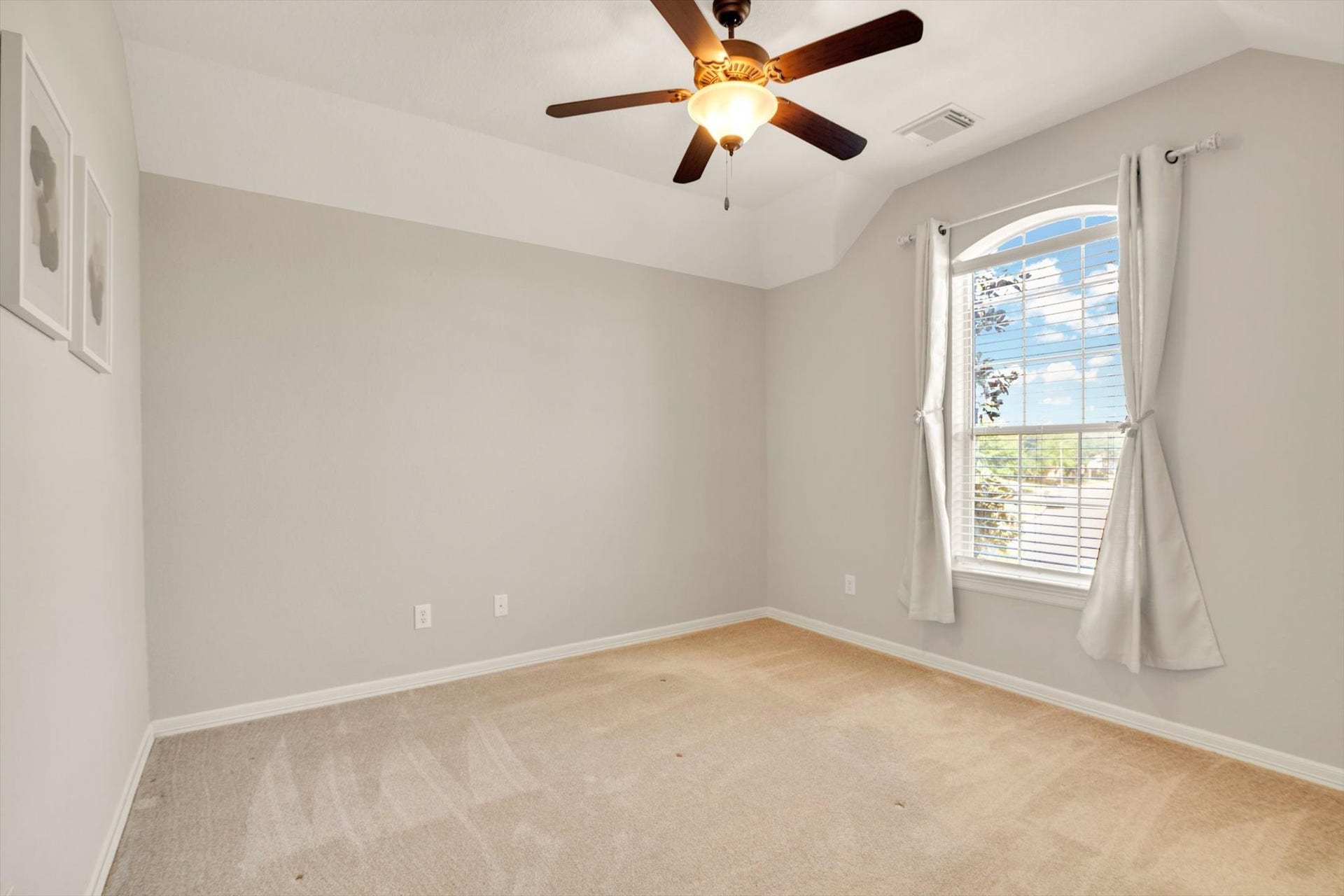 Secondary Bedroom features neutral walls and carpet, a ceiling fan with light, and a large window with drapes, providing plenty of natural light. Perfect for a bedroom or office space.
