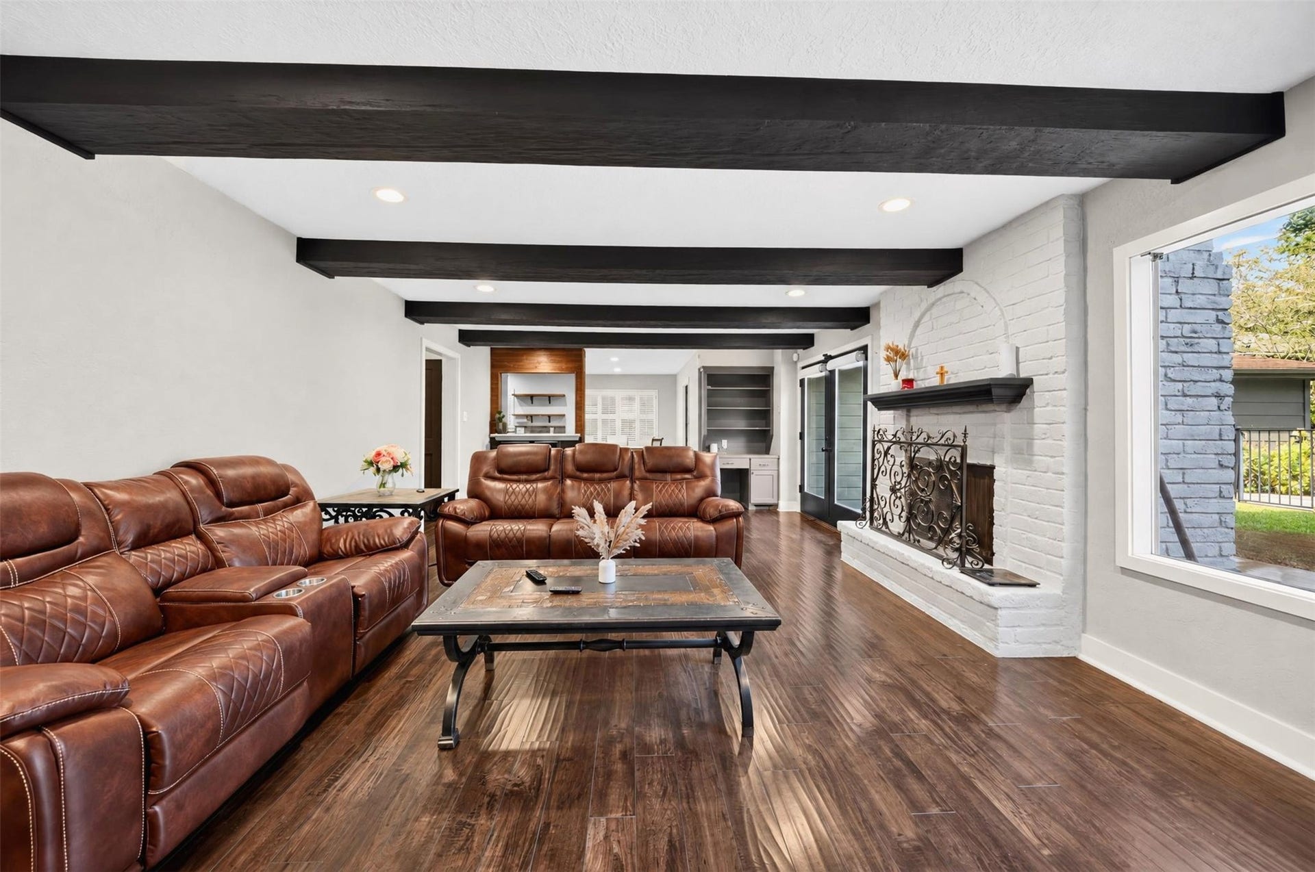 10818 Creektree Drive, Houston, TX 77070 Living Room: Spacious living room featuring rich wood-look flooring, striking exposed ceiling beams, a white brick fireplace, and abundant natural light.