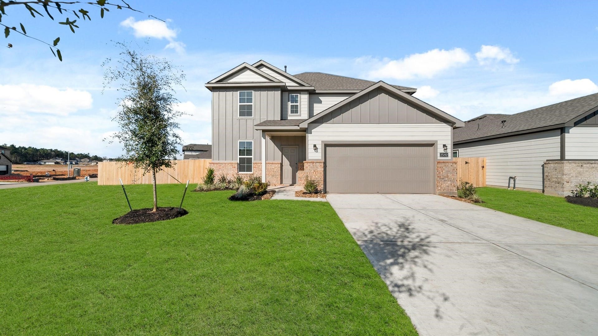 25192 Leather Leaf Court, Montgomery, TX 77316 This photo shows a modern two-story house with a clean, neutral exterior. It features a double garage, a well-maintained lawn, and a fenced backyard. The home is situated in a developing neighborhood, indicated by nearby construction.