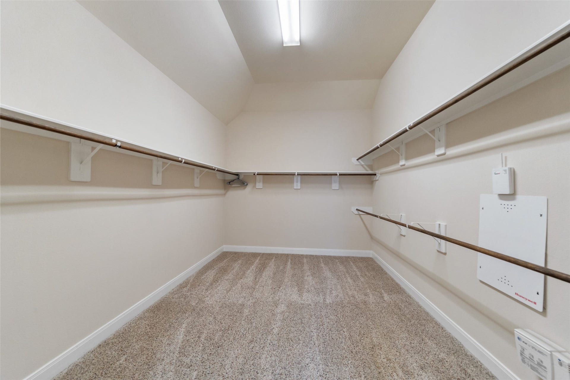 34 Danby Place, The Woodlands, TX 77375 This is a spacious walk-in closet in the primary bedroom featuring multiple hanging rods and shelving, with neutral walls and carpeted flooring, offering ample storage space under bright lighting.