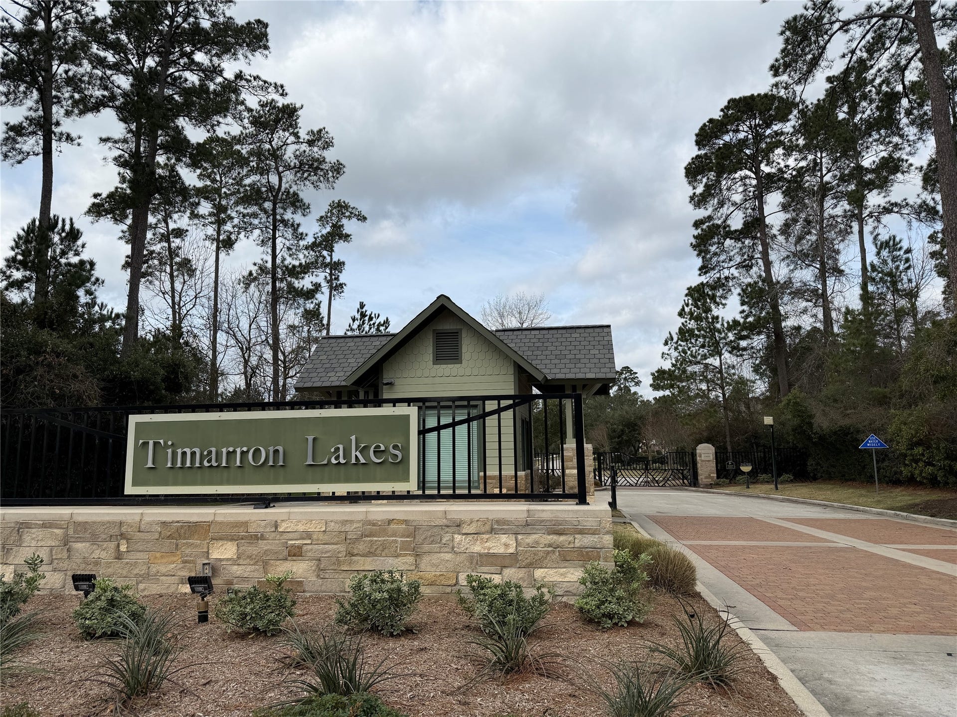 34 Danby Place, The Woodlands, TX 77375 The entrance to Timarron Lakes features a gated entry with a stone sign and lush greenery, suggesting a secure and serene residential community.
