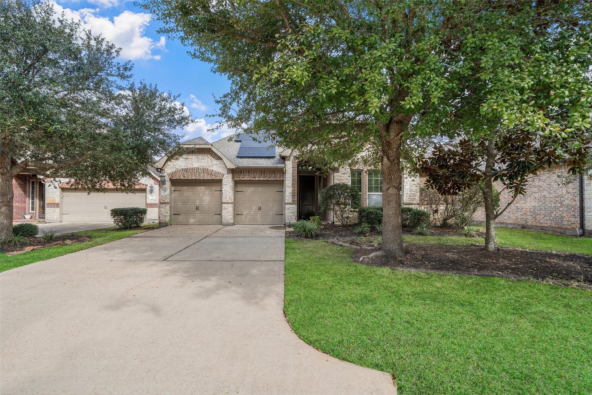 34 Danby Place, The Woodlands, TX 77375 This charming single-story home features a brick and stone exterior, a two-car garage, and a welcoming entryway. The front yard is landscaped with shrubs and trees, and solar panels are installed on the roof, enhancing energy efficiency. Features mature trees and a spacious driveway, offering excellent curb appeal in a quiet neighborhood.