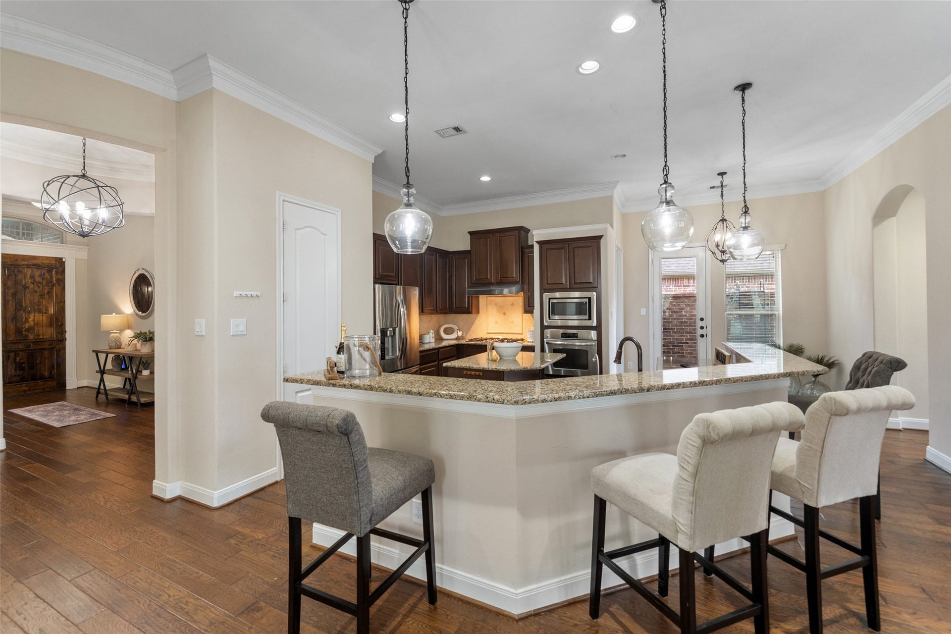 34 Danby Place, The Woodlands, TX 77375 The space is open and airy, featuring stainless steel appliances, dark wood cabinets, and hardwood floors. There's a door leading to an outdoor area, enhancing the room's natural light.