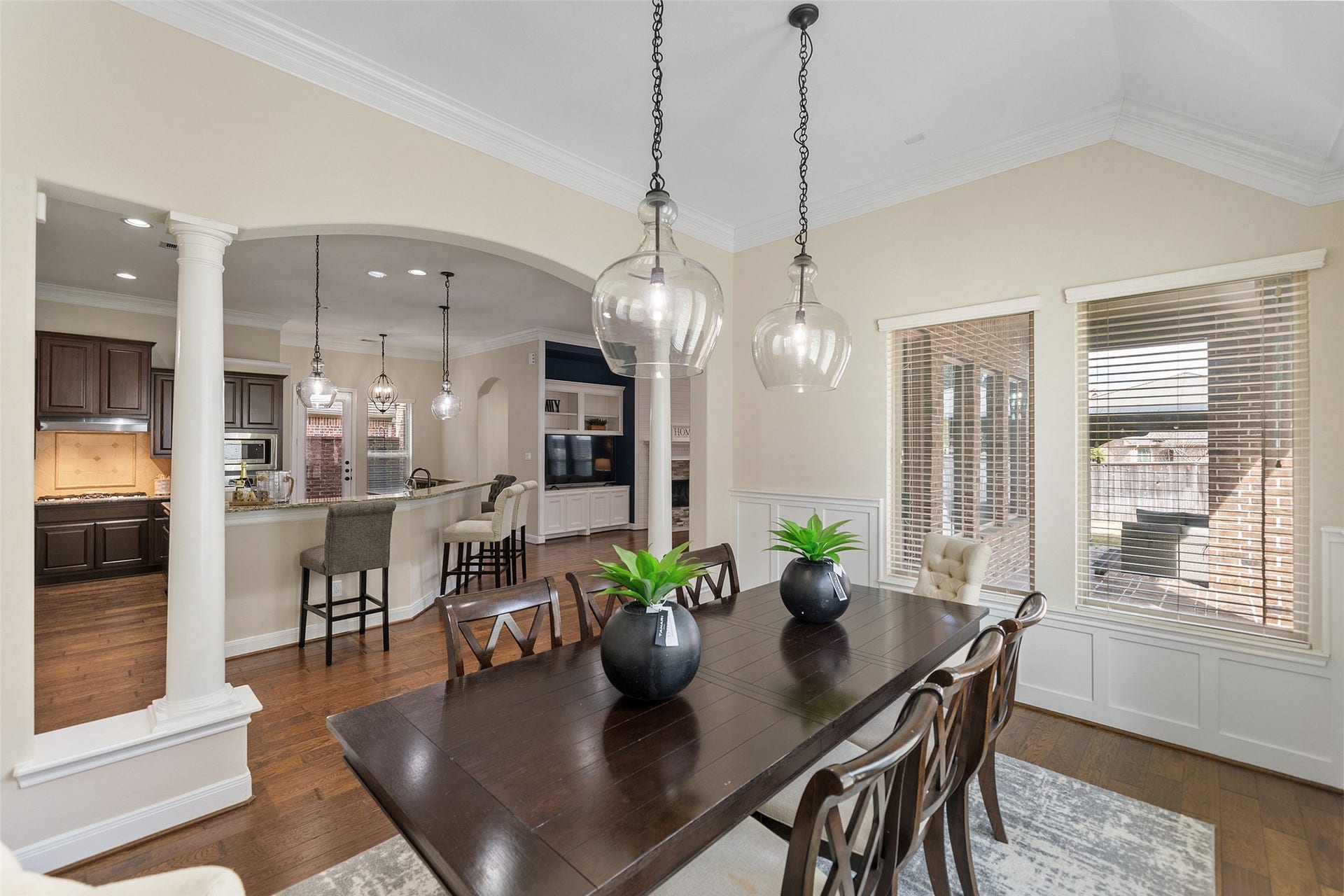34 Danby Place, The Woodlands, TX 77375 The seamlessly dining room flows into a kitchen with dark wood cabinetry and a breakfast bar. The space features hardwood floors and elegant crown molding for a sophisticated touch.