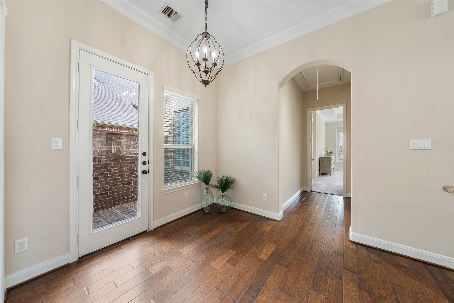 34 Danby Place, The Woodlands, TX 77375 This inviting hallway features hardwood floors, neutral walls, and a stylish light fixture. It includes a glass door leading outside and an archway opening into a carpeted room, perfect for seamless indoor-outdoor flow.