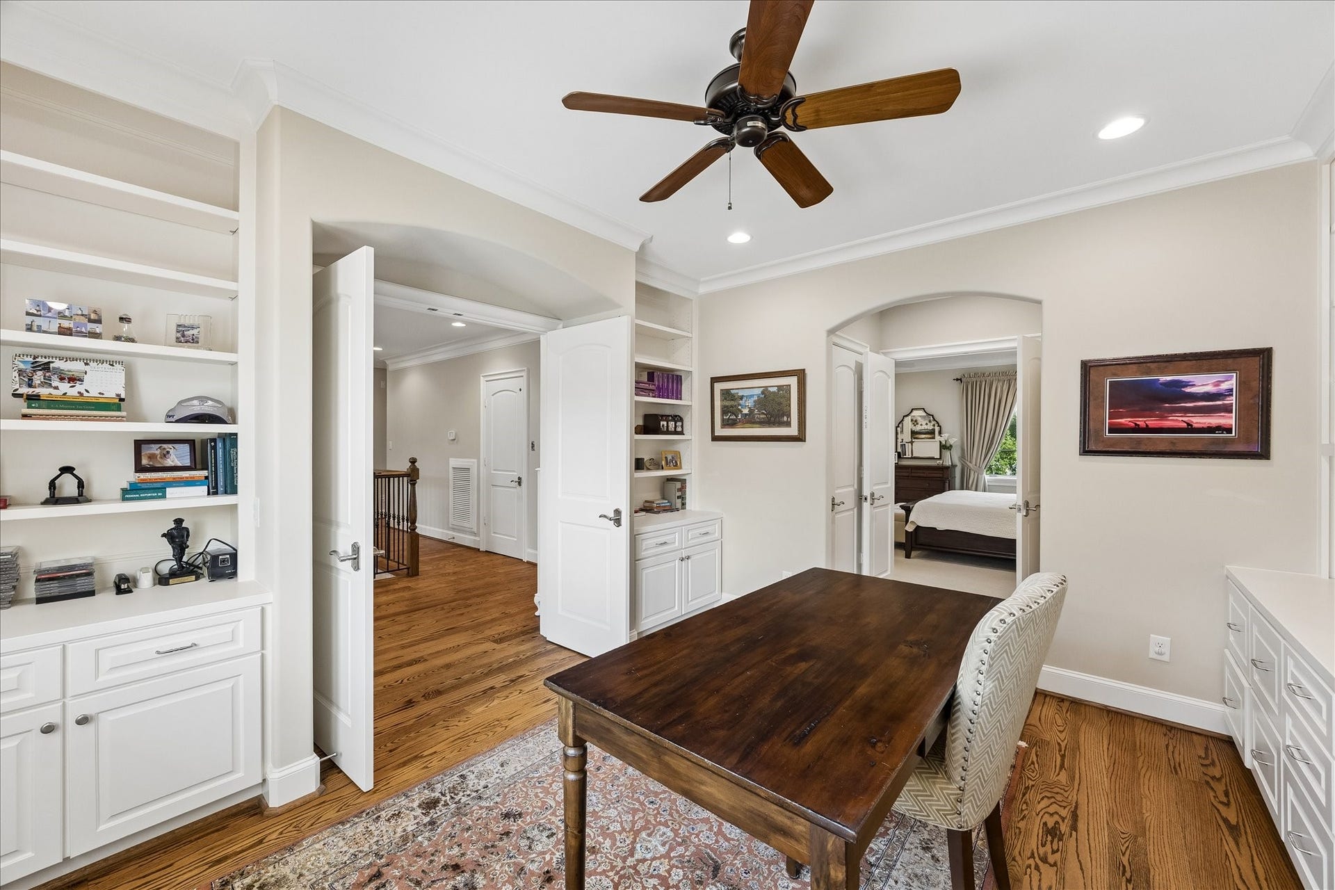 Alternate view from the home office into the primary and second floor landing. Built-in shelving and cabinetry on both sides of the room for display and storage alike.