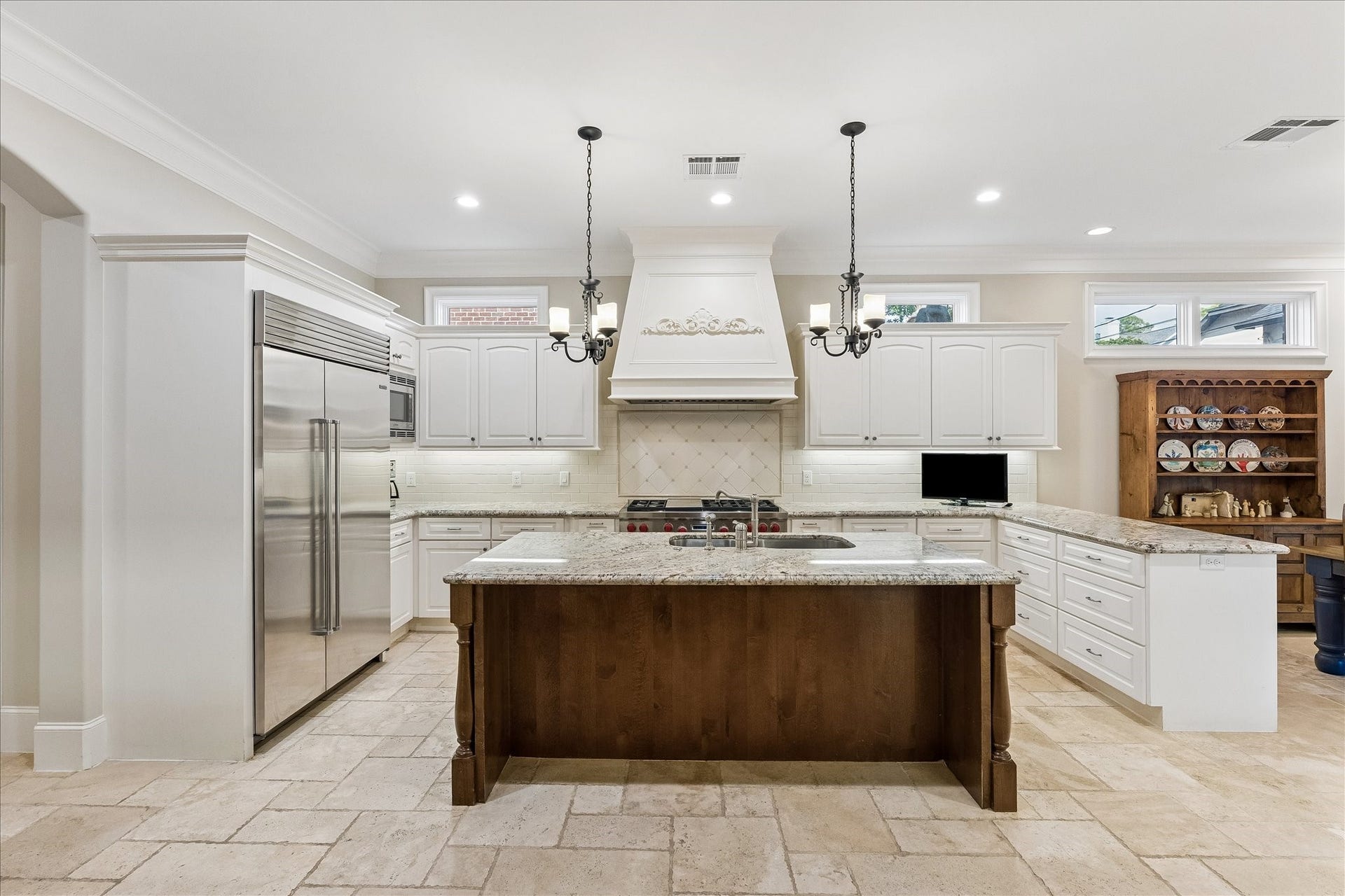 Chef's kitchen featuring travertine floors, SubZero and Wolf appliances, island with double sided sink and transom windows for soft, natural light.