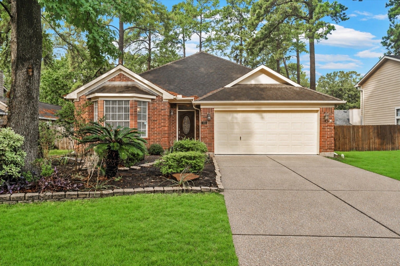 11 Sweetdream Place, The Woodlands, TX 77381 Charming brick home with a welcoming front yard, lush landscaping, and a spacious two-car garage, nestled in a serene neighborhood surrounded by mature trees.