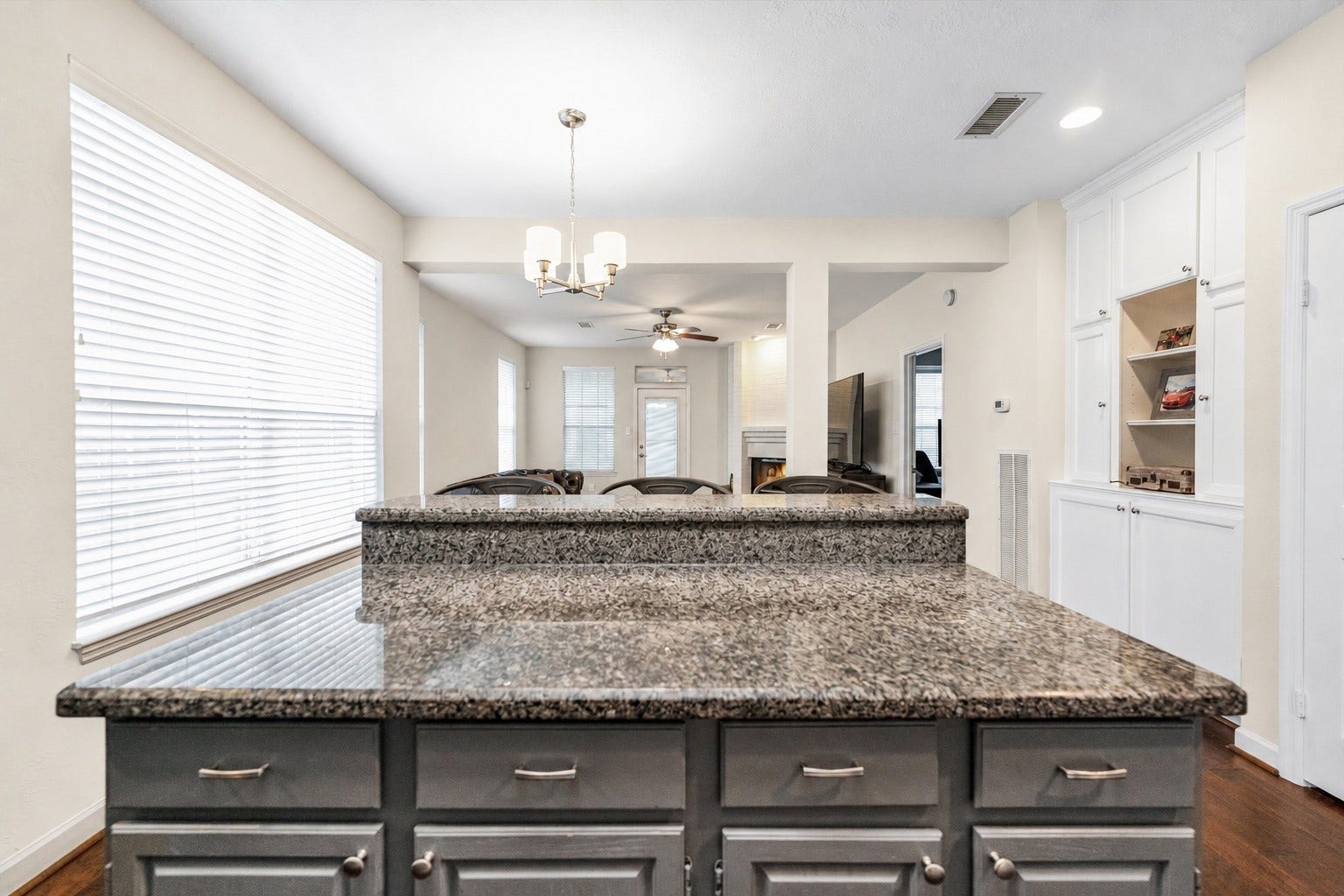 11 Sweetdream Place, The Woodlands, TX 77381 Spacious kitchen featuring a sleek granite island, ample cabinetry, and a view into the bright, open-concept living area with built-in shelving and a cozy fireplace.