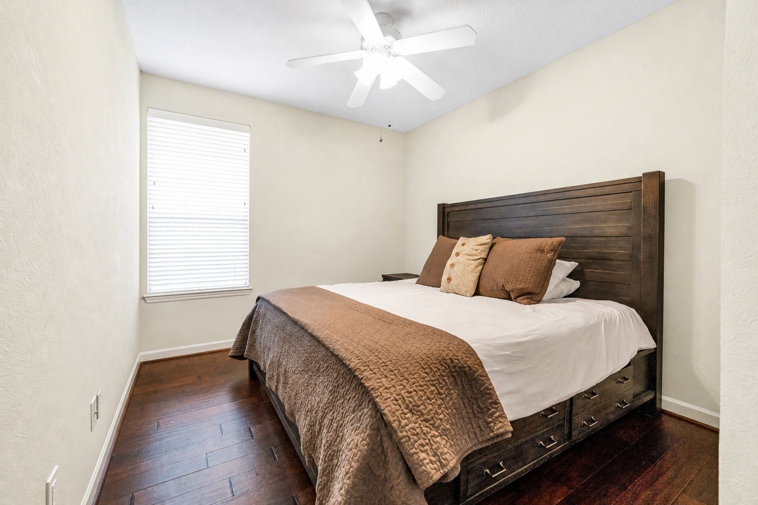 11 Sweetdream Place, The Woodlands, TX 77381 Cozy second bedroom featuring a stylish wooden bed frame, warm bedding, and a bright window, all complemented by elegant hardwood floors.
