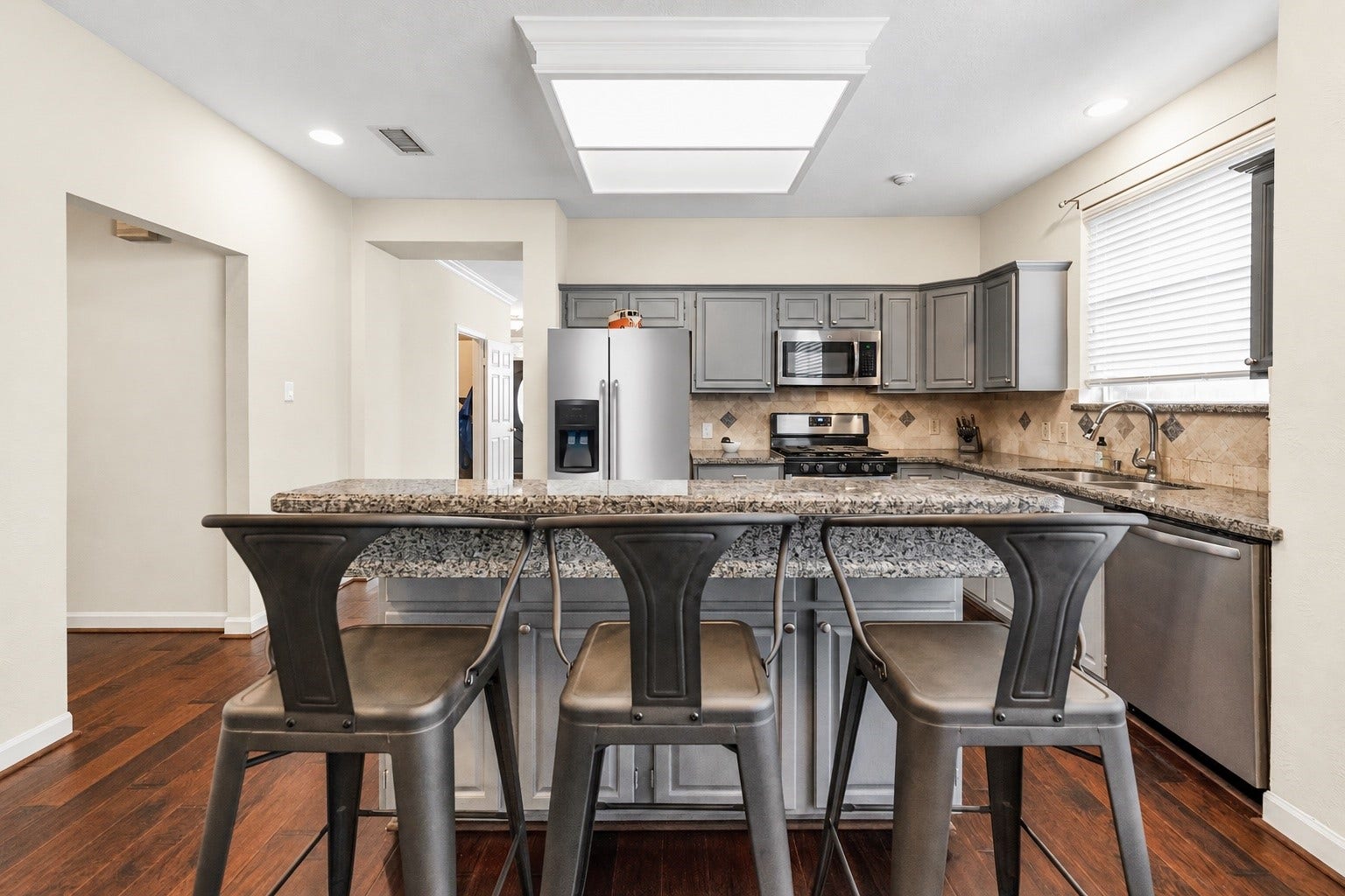 11 Sweetdream Place, The Woodlands, TX 77381 Modern kitchen with sleek granite countertops, stainless steel appliances, and stylish gray cabinetry, complemented by a cozy breakfast bar with seating.