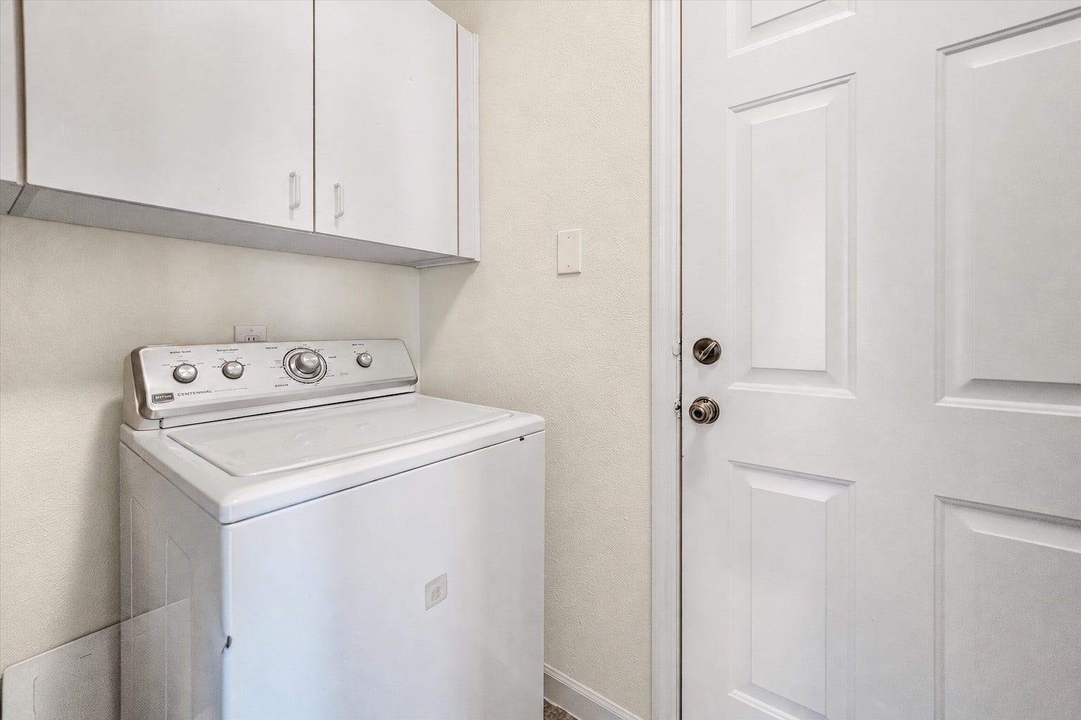 11 Sweetdream Place, The Woodlands, TX 77381 Compact laundry area featuring a top-loading washing machine and overhead storage cabinets, conveniently located next to an exterior door.