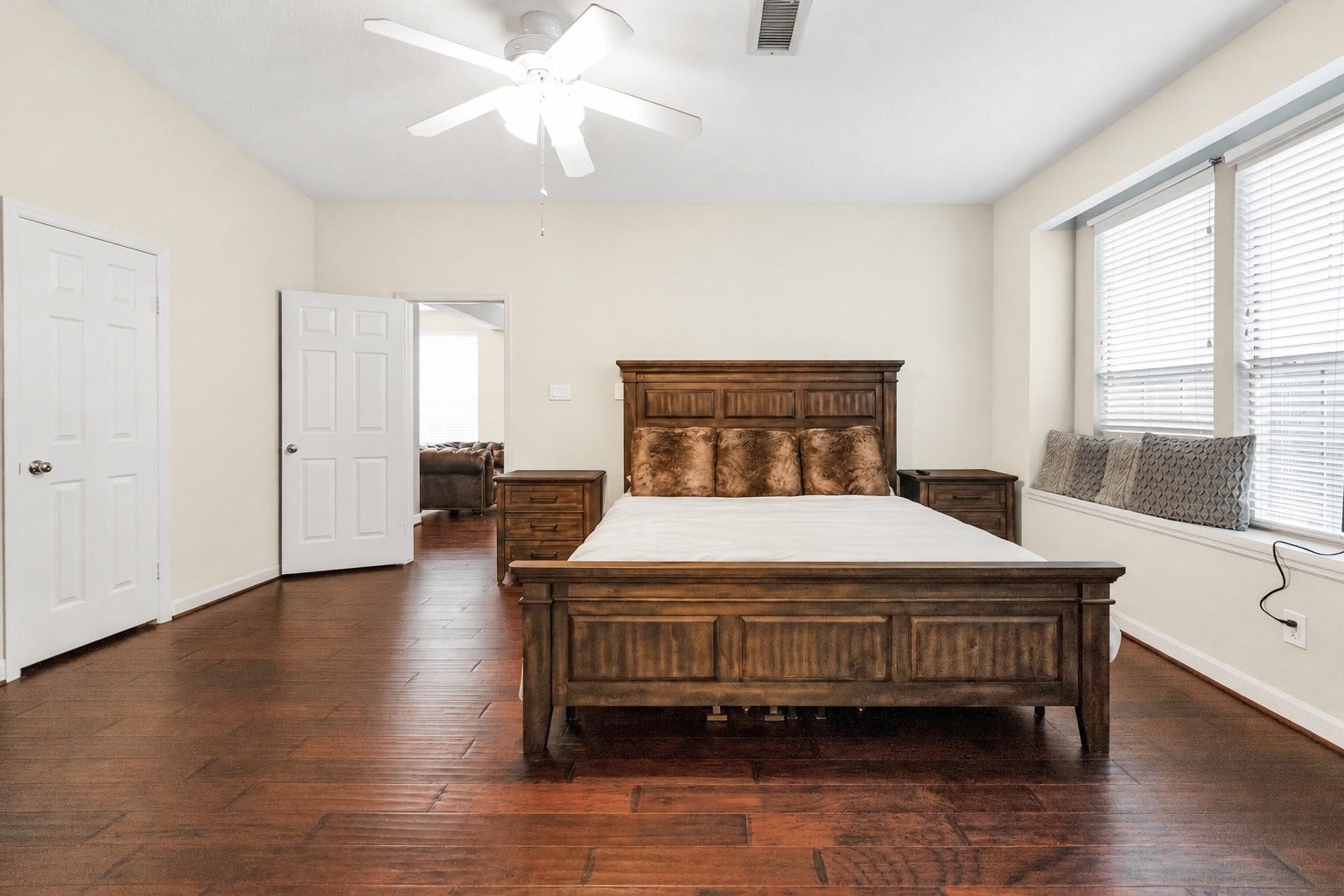 11 Sweetdream Place, The Woodlands, TX 77381 Spacious main bedroom with elegant hardwood floors, featuring a large wooden bed, ample natural light from multiple windows, and a charming window seat for relaxation.