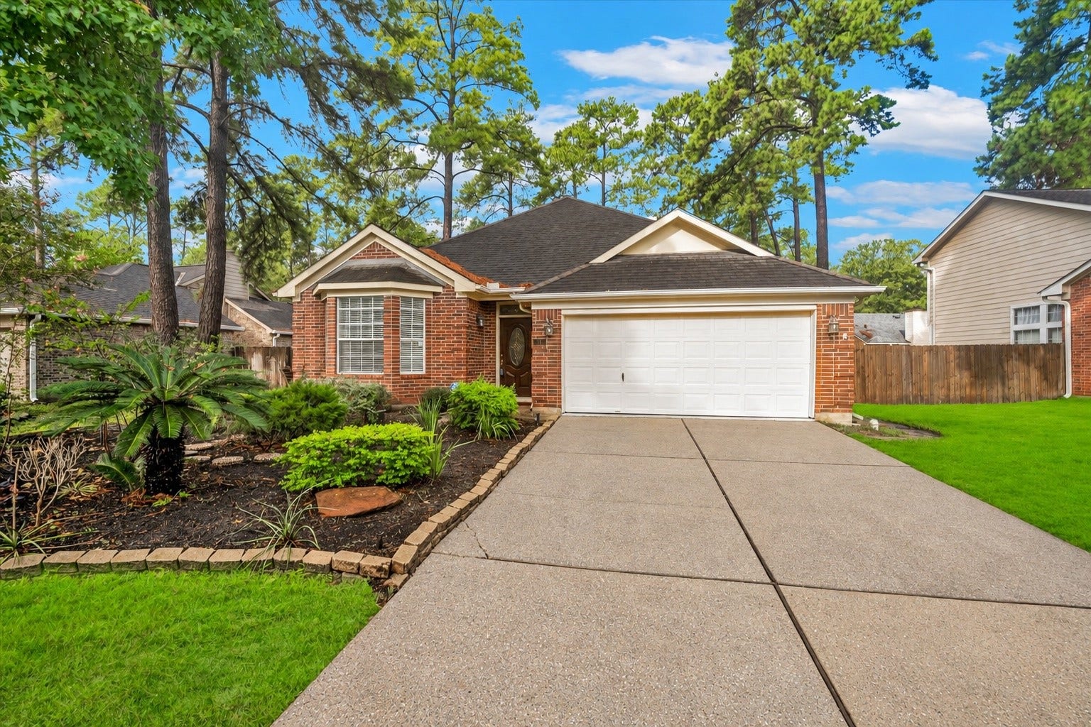11 Sweetdream Place, The Woodlands, TX 77381 Charming brick home with a welcoming front yard and lush landscaping, featuring a spacious driveway leading to a two-car garage.