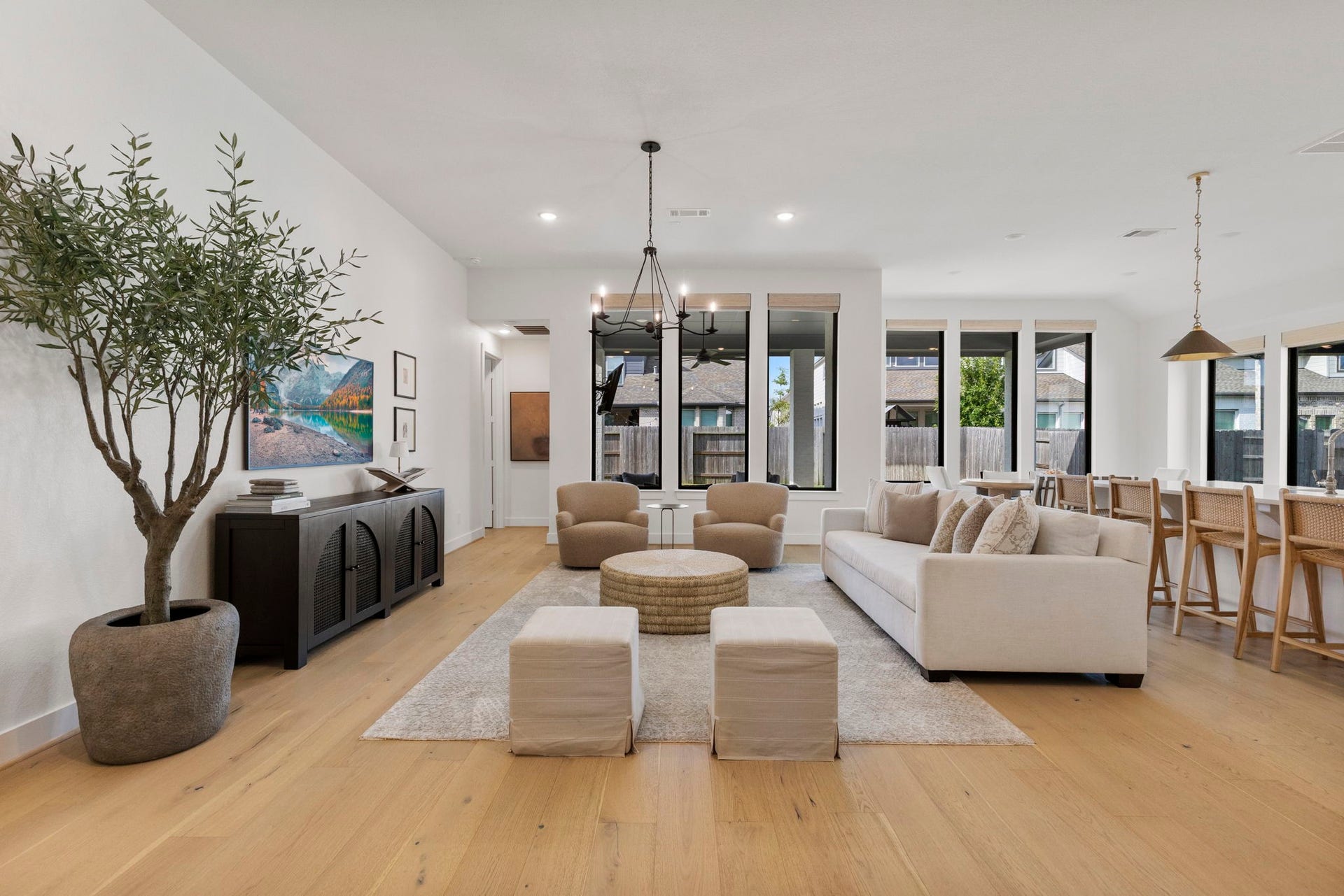 18030 Blu Terrace Drive, Conroe, TX 77302 Sunlit open living room with hardwood floors, modern chandelier, and tall picture windows overlooking the patio.