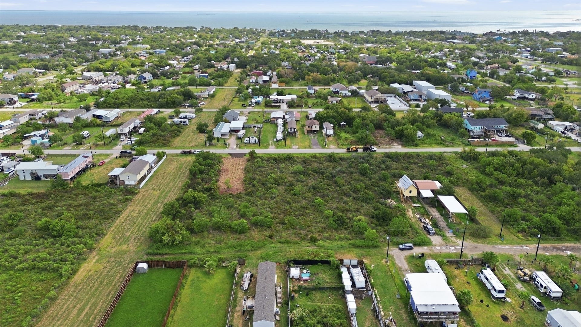 17 W Street, San Leon, TX 77539 Aerial view from above the road looking across the property toward Galveston Bay. A cleared pad with a gravel driveway apron sits at the road frontage. Established neighborhood homes line the street across the way.