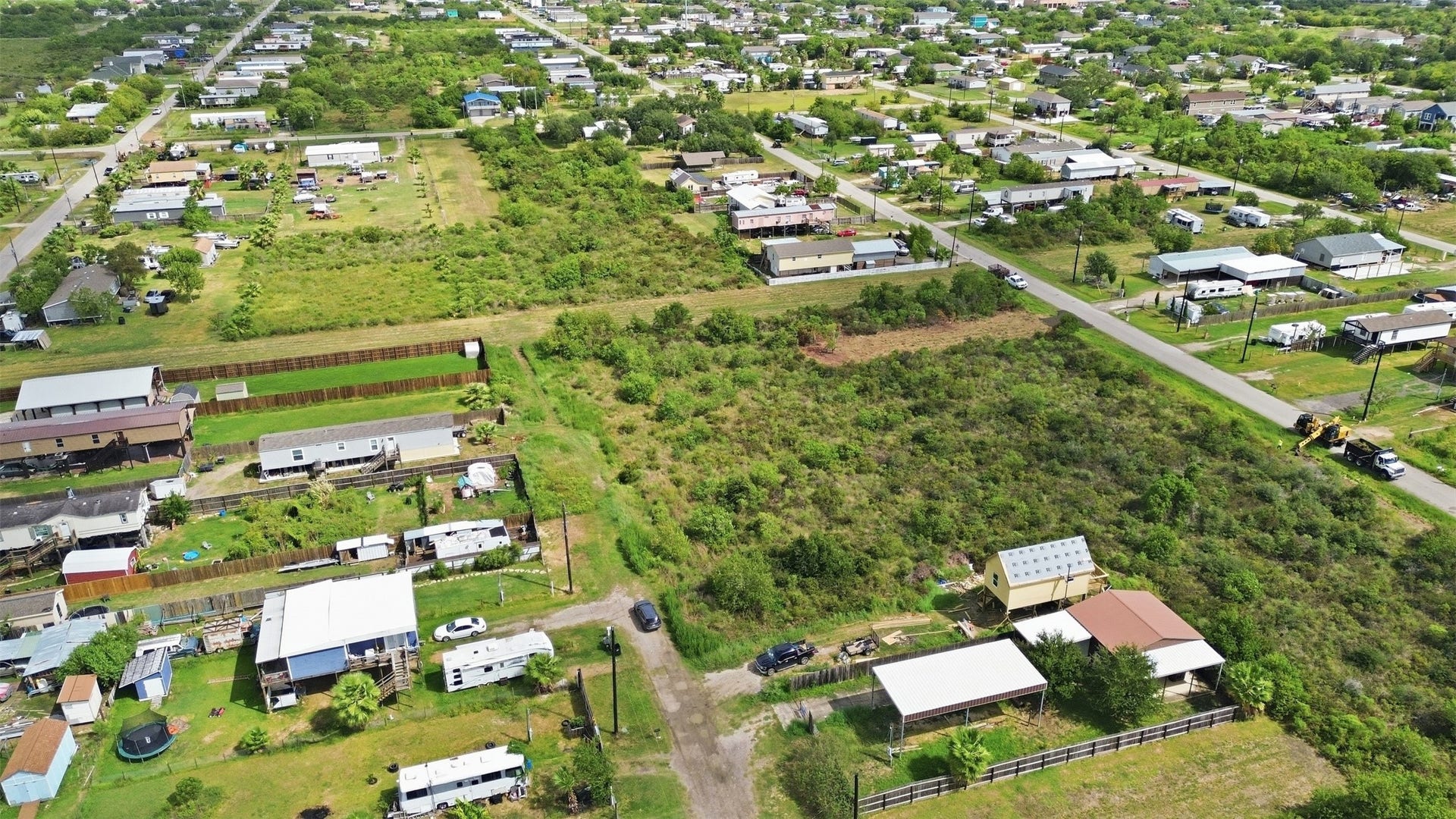 17 W Street, San Leon, TX 77539 Aerial from the rear of the property looking out over the neighborhood. A gravel access road runs along one side, and the paved street is at the far edge.