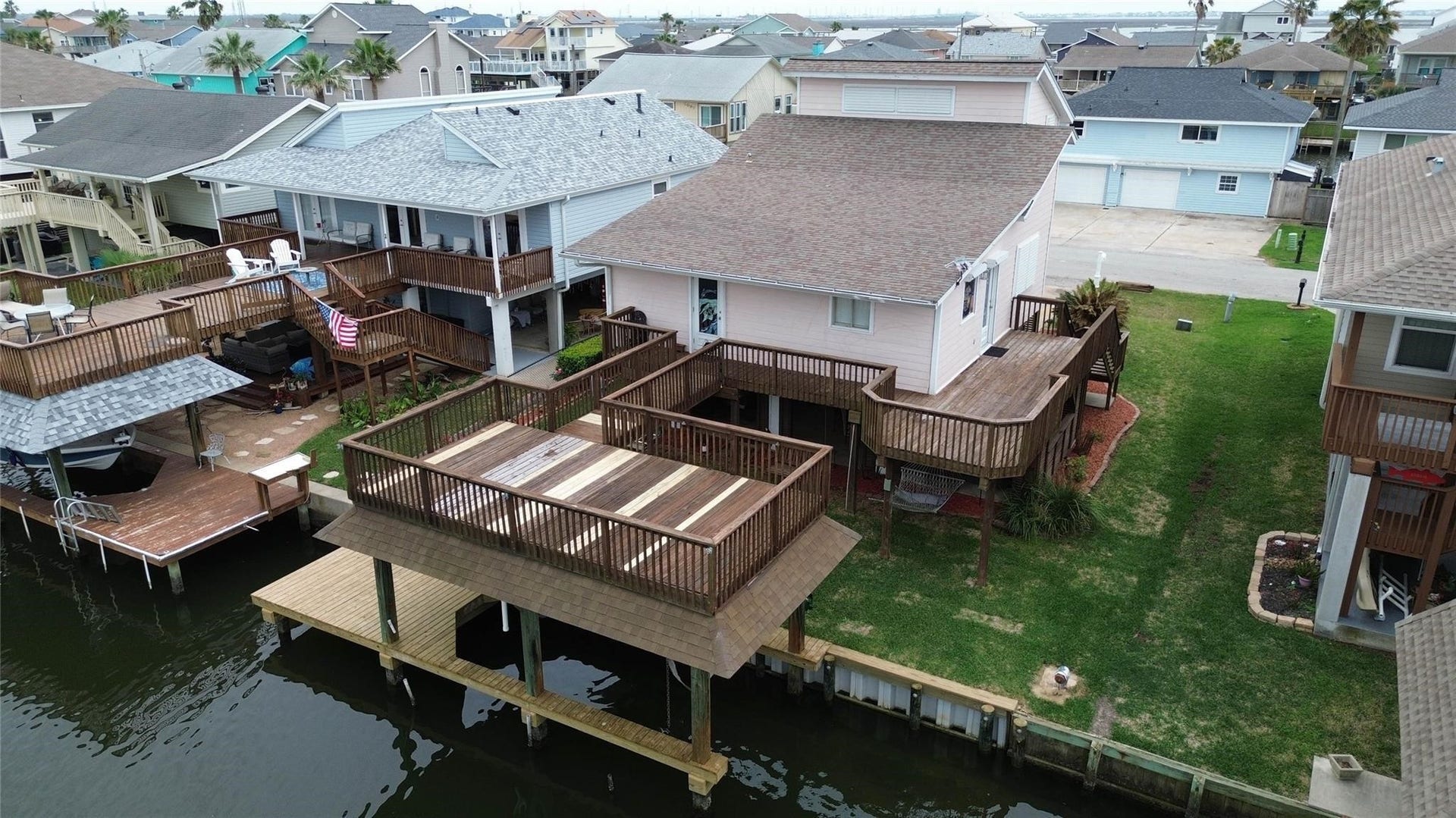 1031 Redfish Street, Bayou Vista, TX 77563 This waterfront home features a spacious deck overlooking a canal, providing direct water access. The house has a large wooden patio and a well-maintained lawn, perfect for outdoor activities and relaxation. The surrounding neighborhood consists of similar homes, creating a pleasant, coastal community atmosphere.