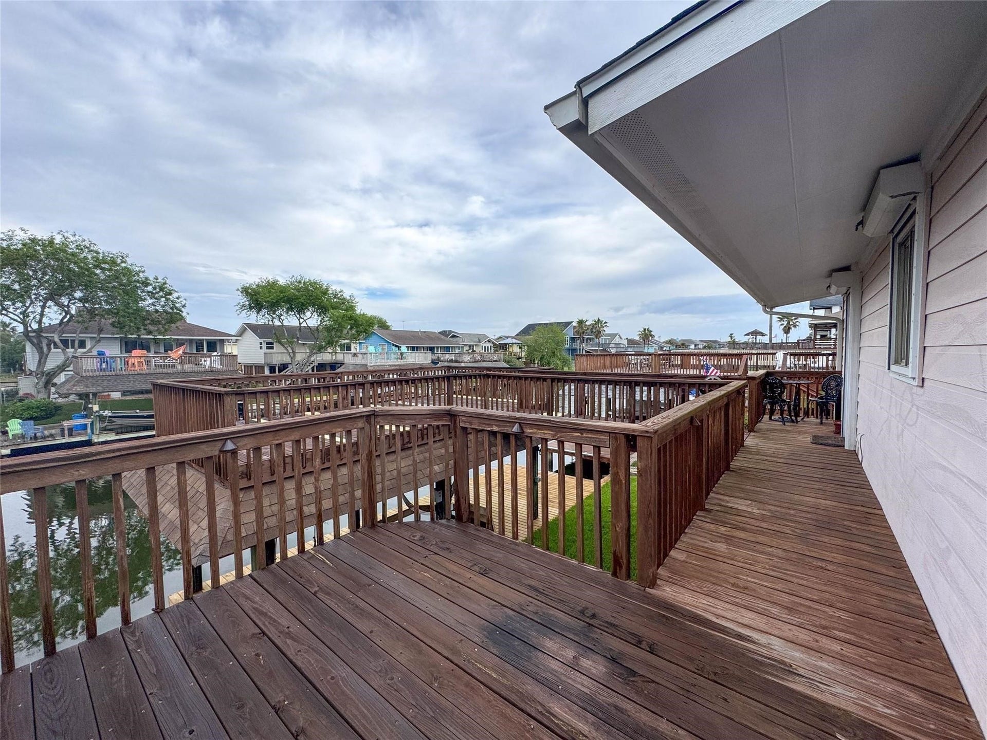 1031 Redfish Street, Bayou Vista, TX 77563 This photo showcases a waterside home with a spacious wooden deck overlooking a canal, ideal for outdoor relaxation. The surrounding neighborhood features similar waterfront properties, providing a serene and picturesque setting.