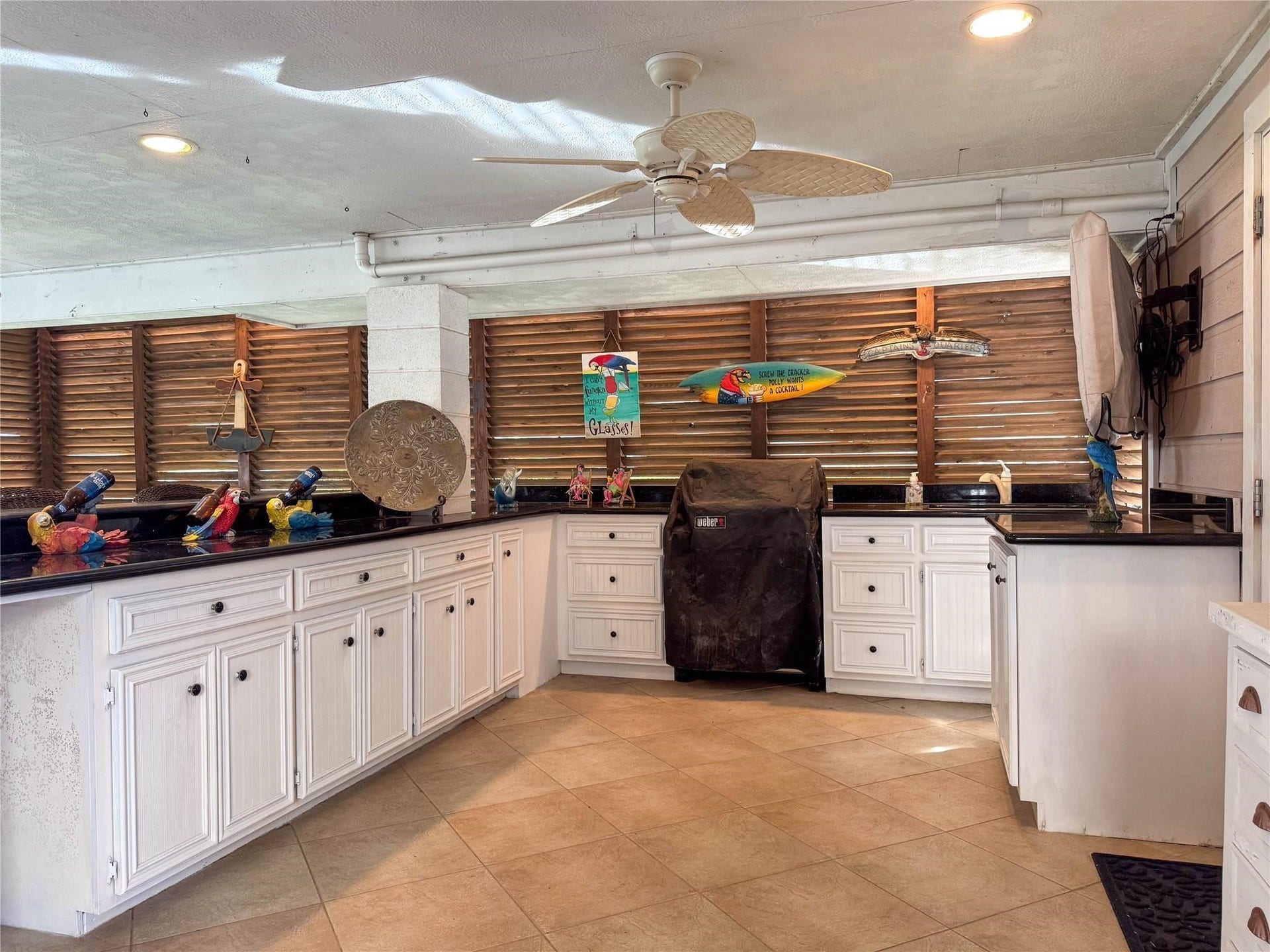 1031 Redfish Street, Bayou Vista, TX 77563 This photo showcases an inviting outdoor kitchen with ample counter space, white cabinetry, and decorative accents. The area includes a covered grill, ceiling fan, and wooden shutters, creating a relaxed, tropical atmosphere perfect for entertaining.