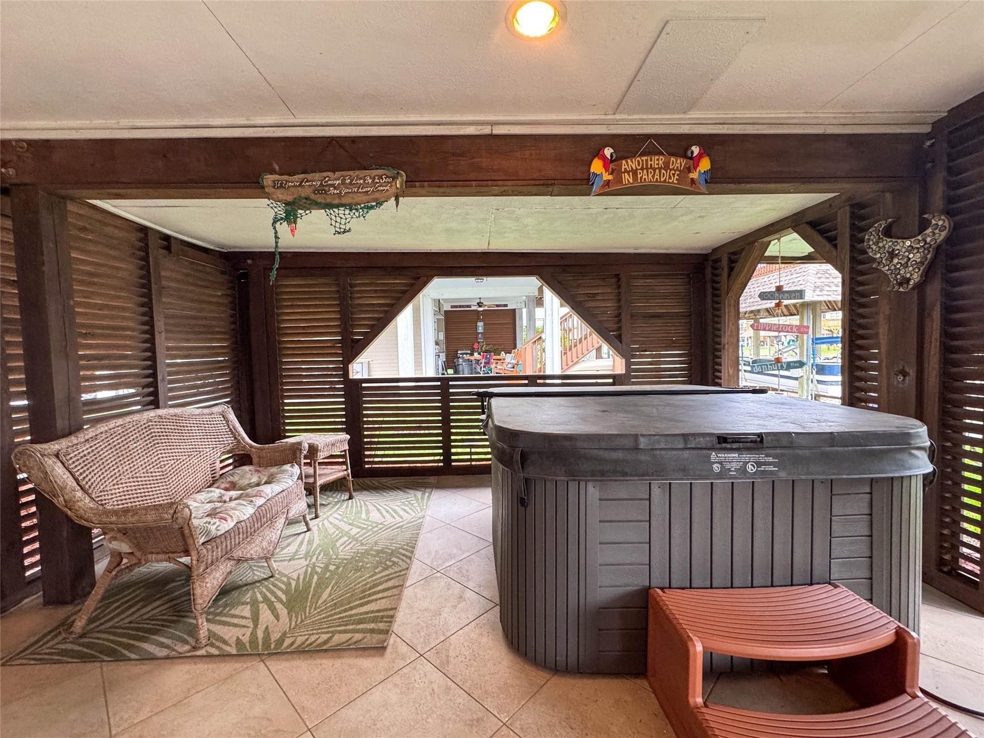 1031 Redfish Street, Bayou Vista, TX 77563 This cozy screened-in porch features a hot tub, wicker seating, and a tropical rug, perfect for relaxation. The wooden accents and decor create a laid-back, paradise-inspired atmosphere.