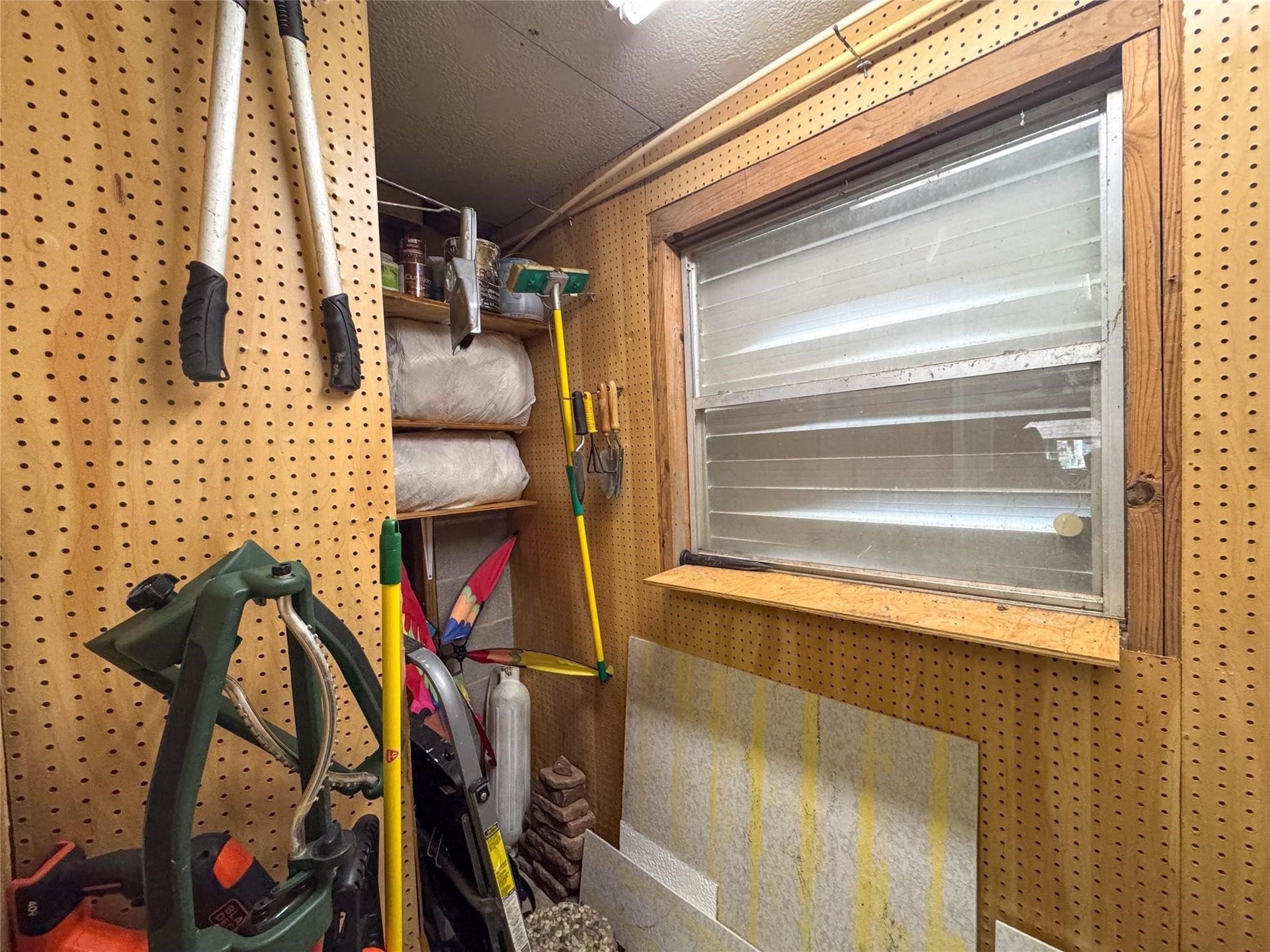 1031 Redfish Street, Bayou Vista, TX 77563 This photo shows a compact storage space with pegboard walls, holding various tools and supplies. A small window provides some natural light, and shelves offer additional storage. Ideal for organizing garden or household tools.