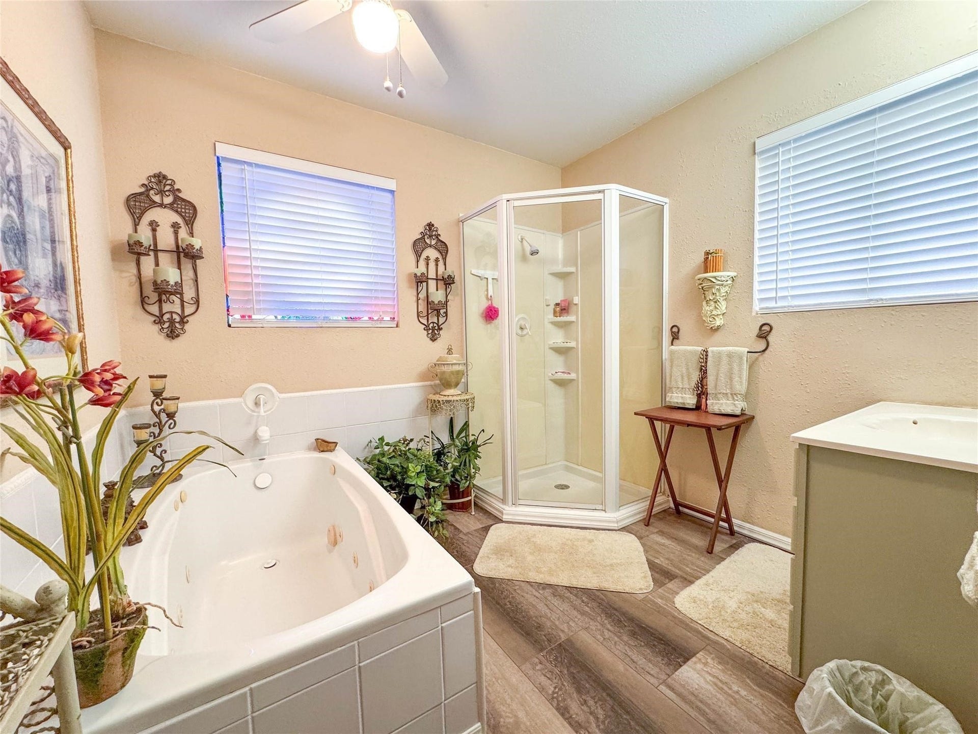 1031 Redfish Street, Bayou Vista, TX 77563 This bathroom features a cozy layout with a corner shower, a spacious soaking tub, and tasteful decor. It has warm beige walls, wood-style flooring, and ample natural light from two windows, creating a relaxing atmosphere.