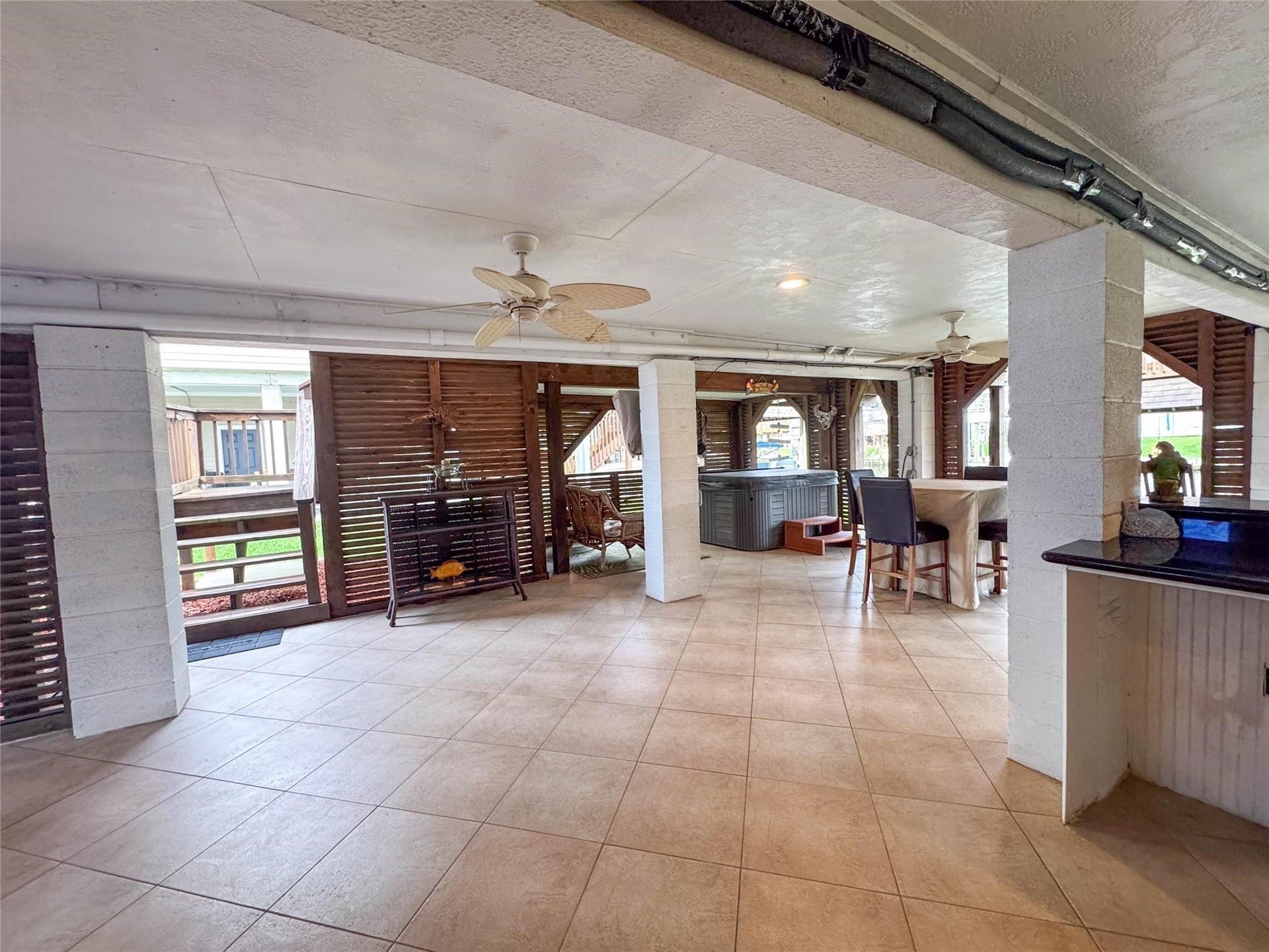 1031 Redfish Street, Bayou Vista, TX 77563 This spacious covered patio features tiled flooring, ceiling fans, and ample seating areas, perfect for outdoor entertaining. The space includes a bar area and a hot tub, with wooden privacy screens providing a cozy and inviting atmosphere.